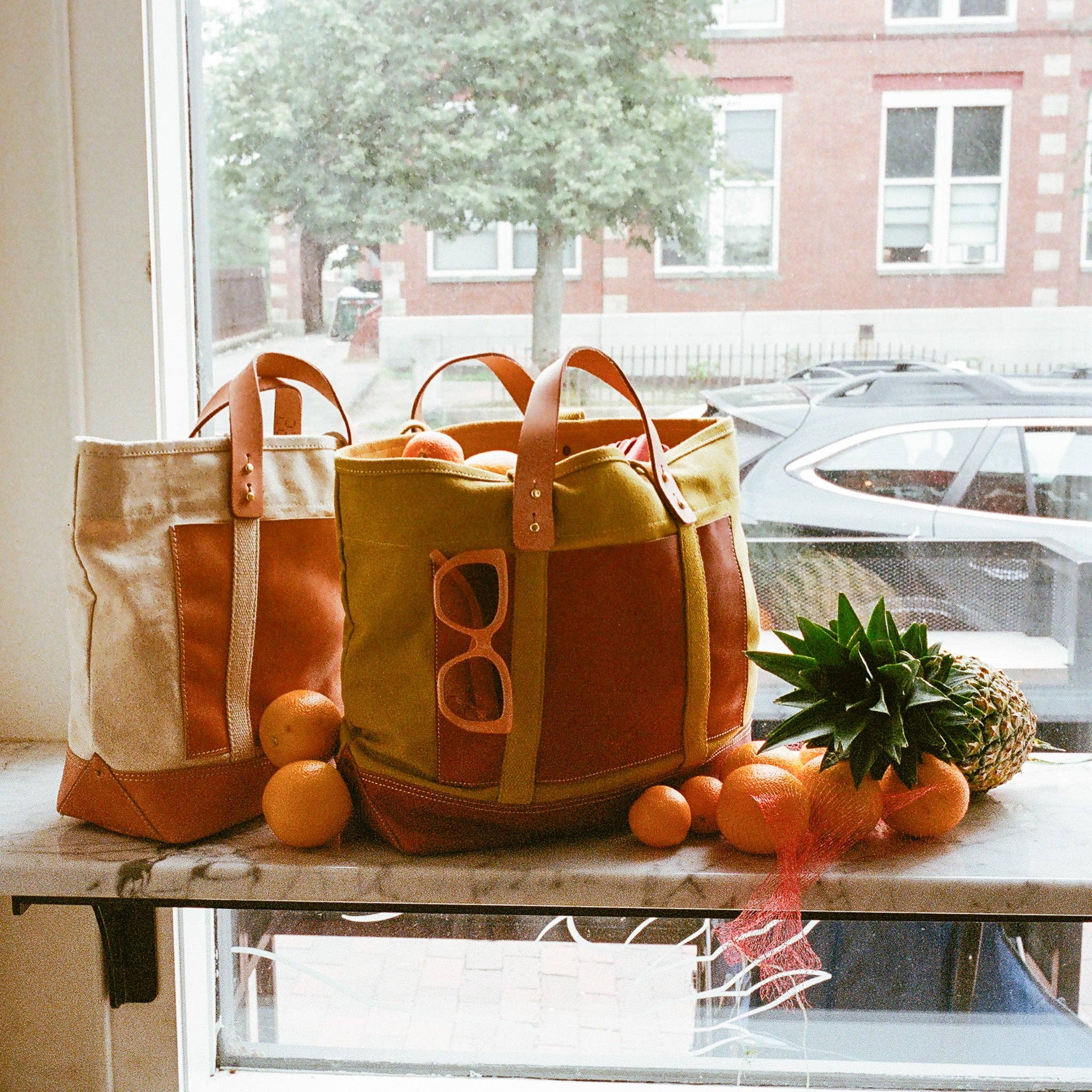Editor Tote | Chartreuse + Bordeaux with leather handles displayed on a window ledge with fruit and sunglasses nearby