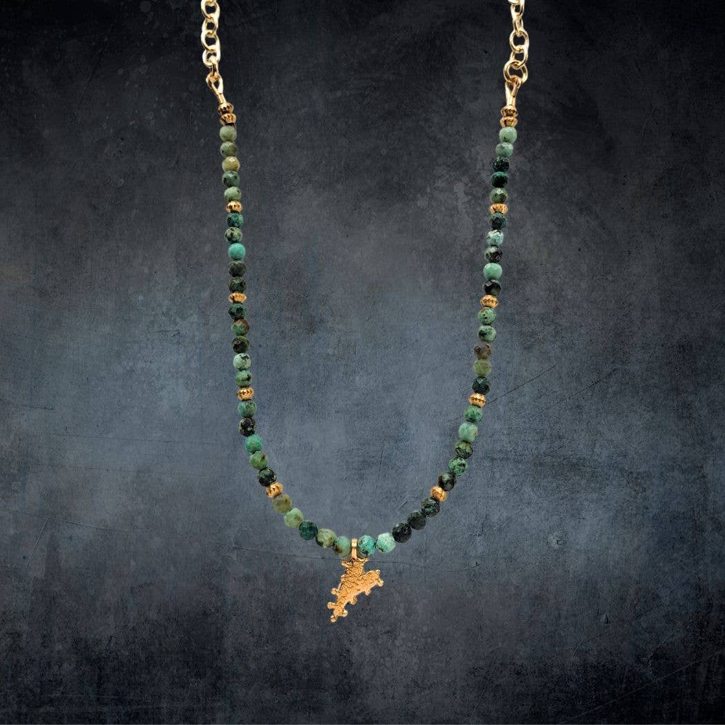 The Chrysocolla Beaded Heart Charm Necklace by Dreamers of Dreams features green and gold beads with a heart charm, displayed on a dark textured background—an ideal piece for any bohemian jewelry collection.