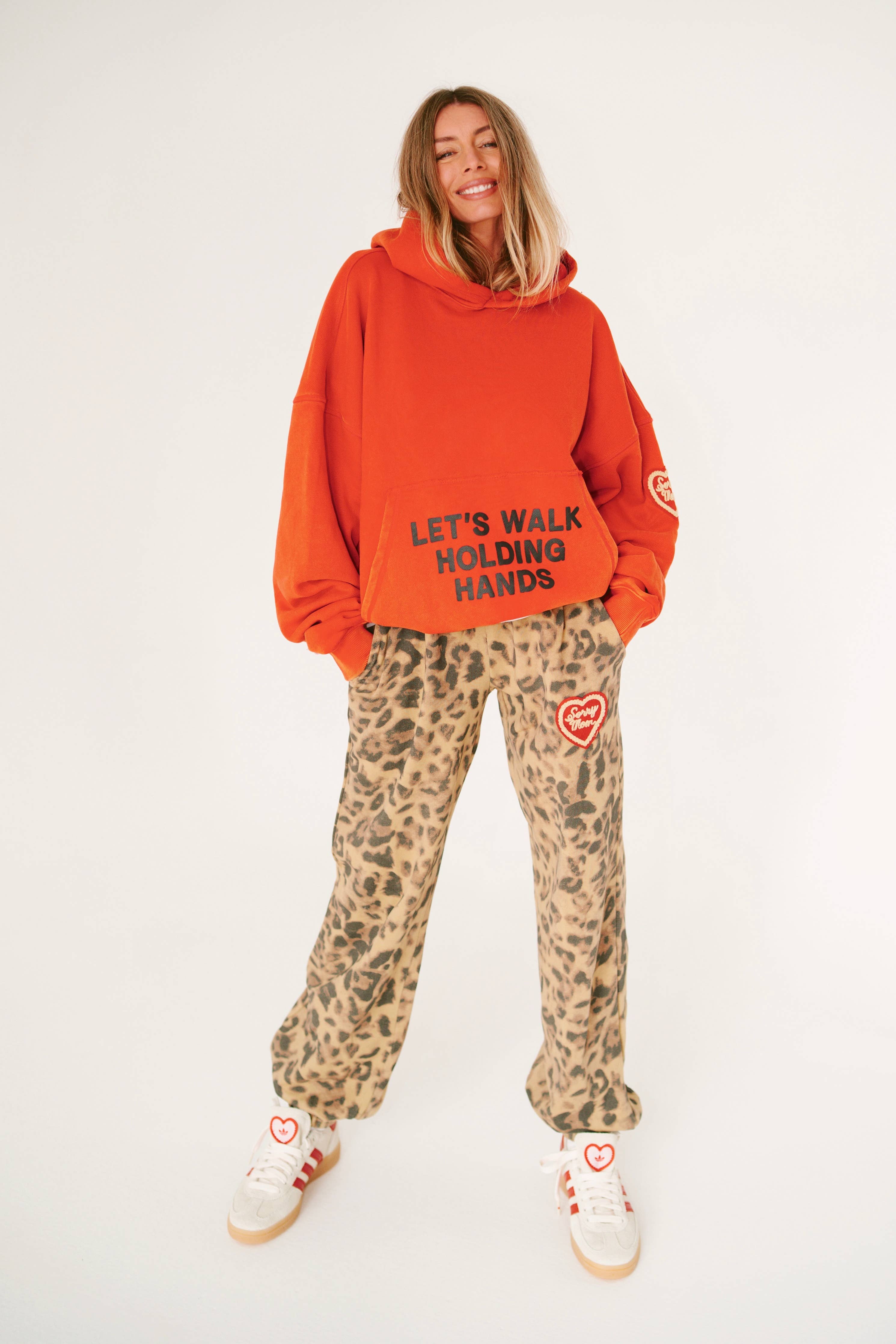 Woman wearing bright orange SORRY MOM HOODIE - PRESALE with leopard print pants and smiling confidently