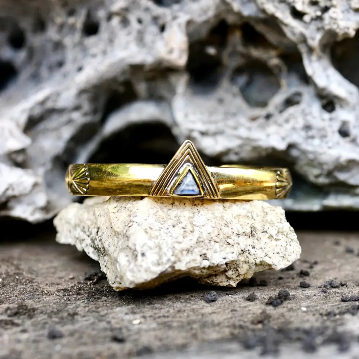 Hold Space Cuff with a gold finish and triangle stone detail resting on textured natural rock background