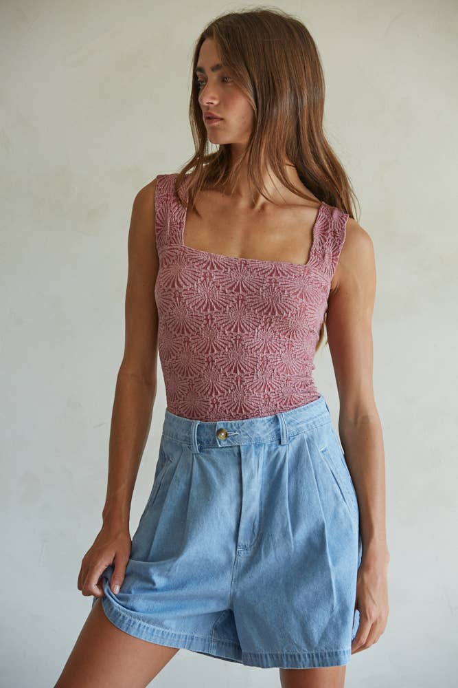 A woman in a By Together Knit Modal Nylon Spandex Seamless Jacquard Tank and high-waisted light blue denim shorts stands against a plain, light-colored wall, looking to the side.