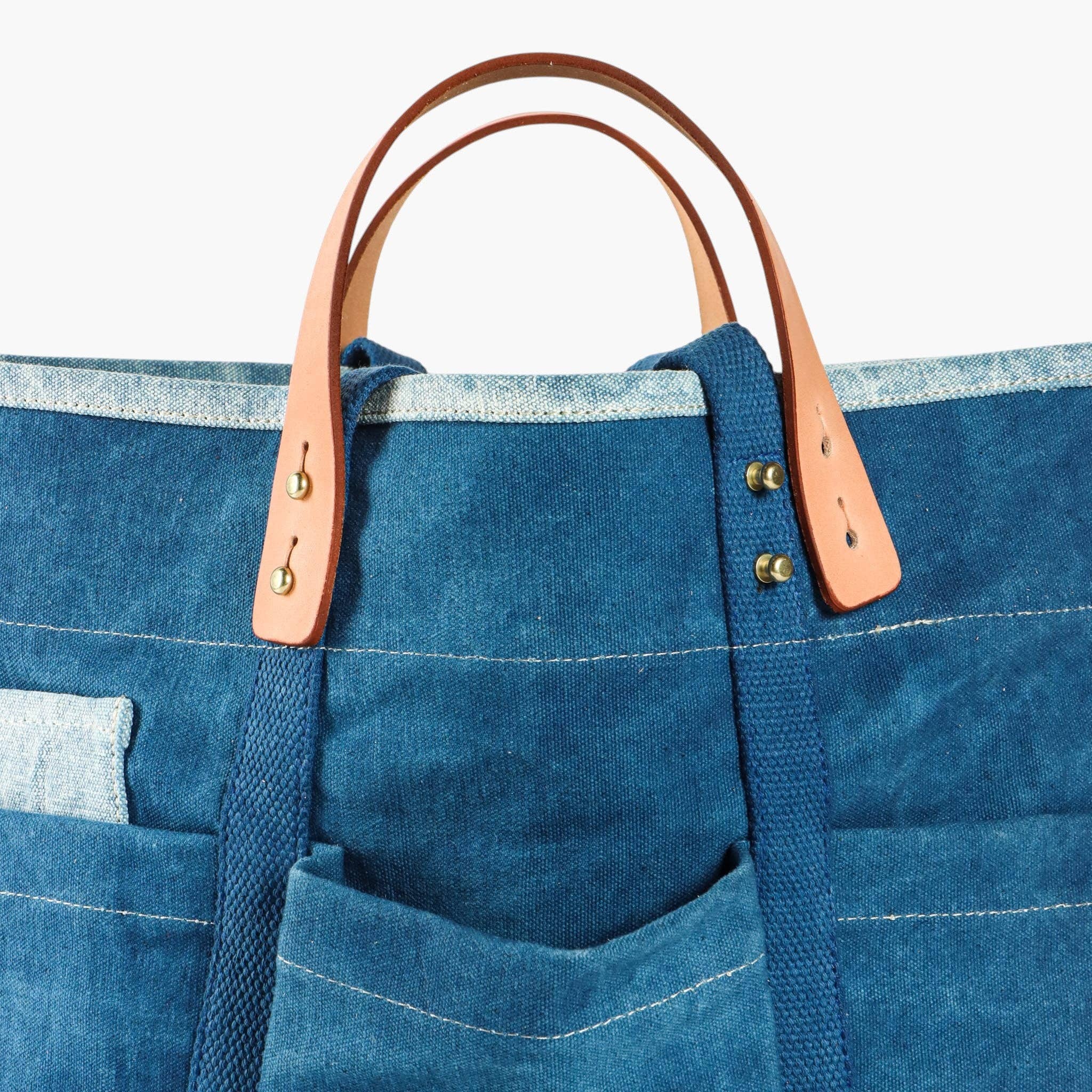 Blue tote bag with brown leather handles on a white background