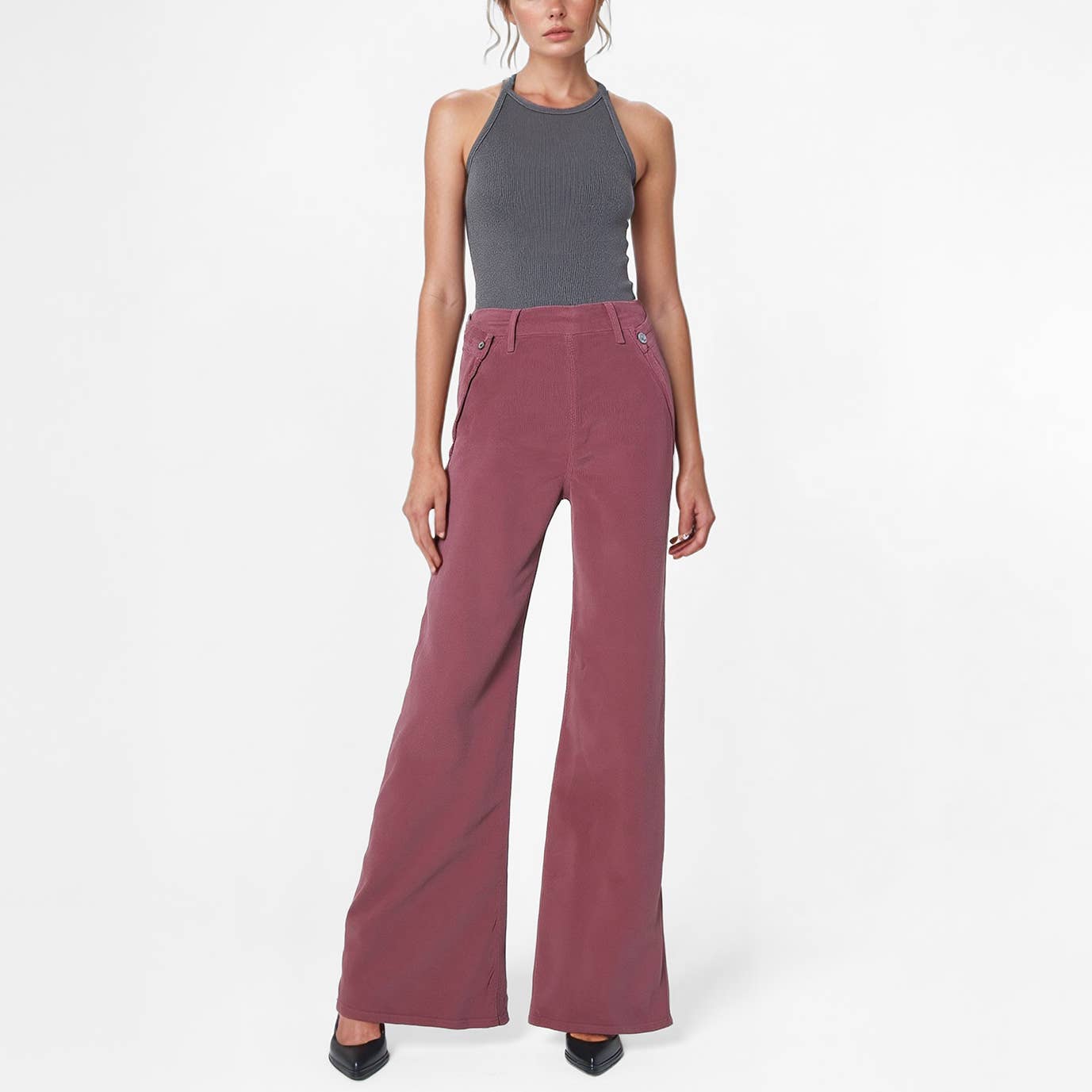 A woman stands against a white background wearing a gray halter top and Noend Denim's Dina High Waisted Wide Corduroy pants in Deep Merlot, styled with black pointed-toe heels.