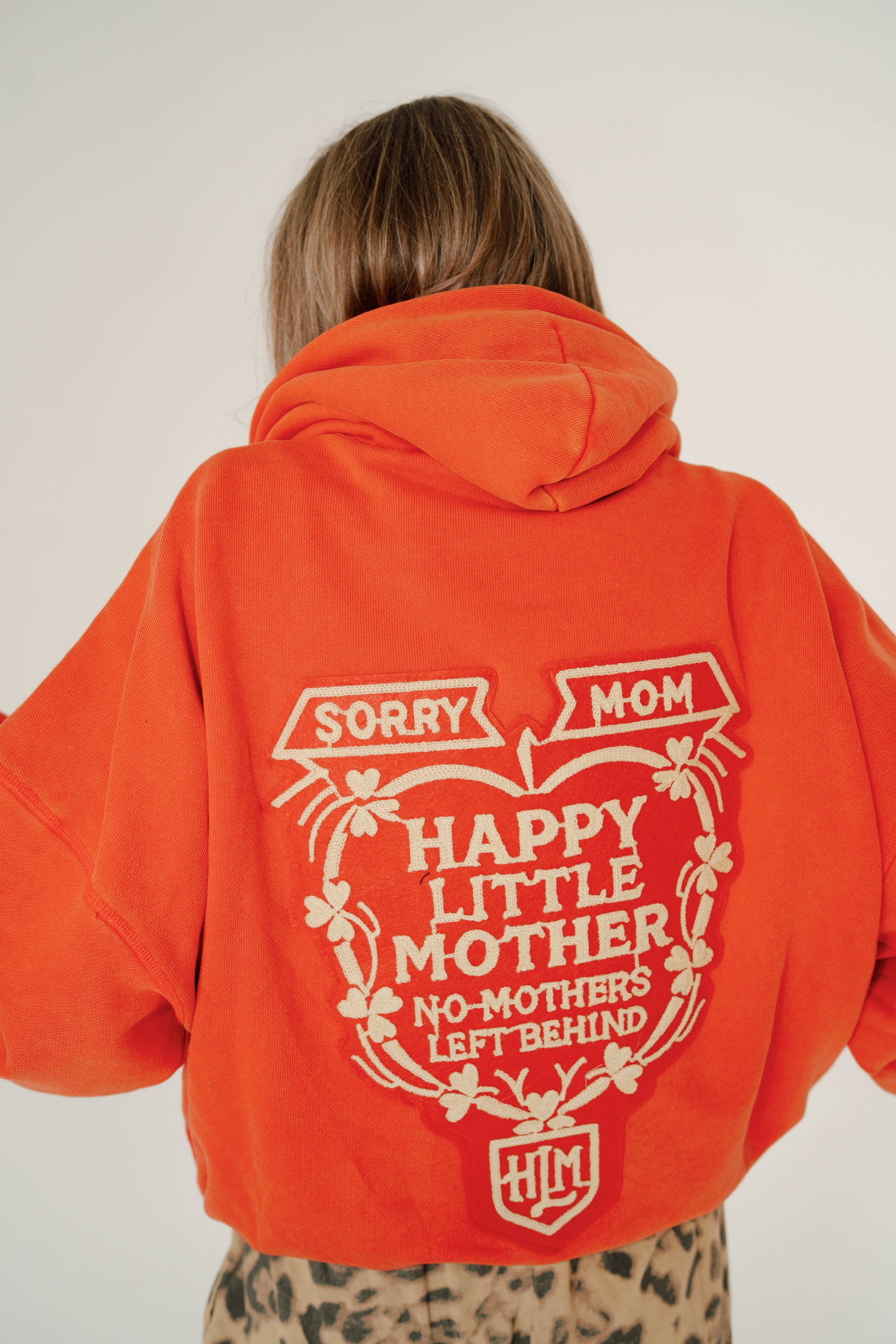 Back view of a person wearing an orange SORRY MOM HOODIE - PRESALE with bold white graphic text and floral design.