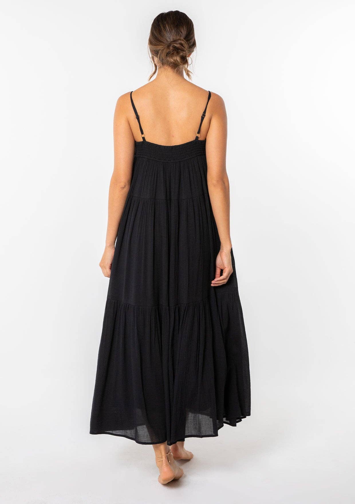 Woman wearing a black Bohemian Crochet Tiered Maxi Dress with thin straps, shown from the back, standing barefoot.