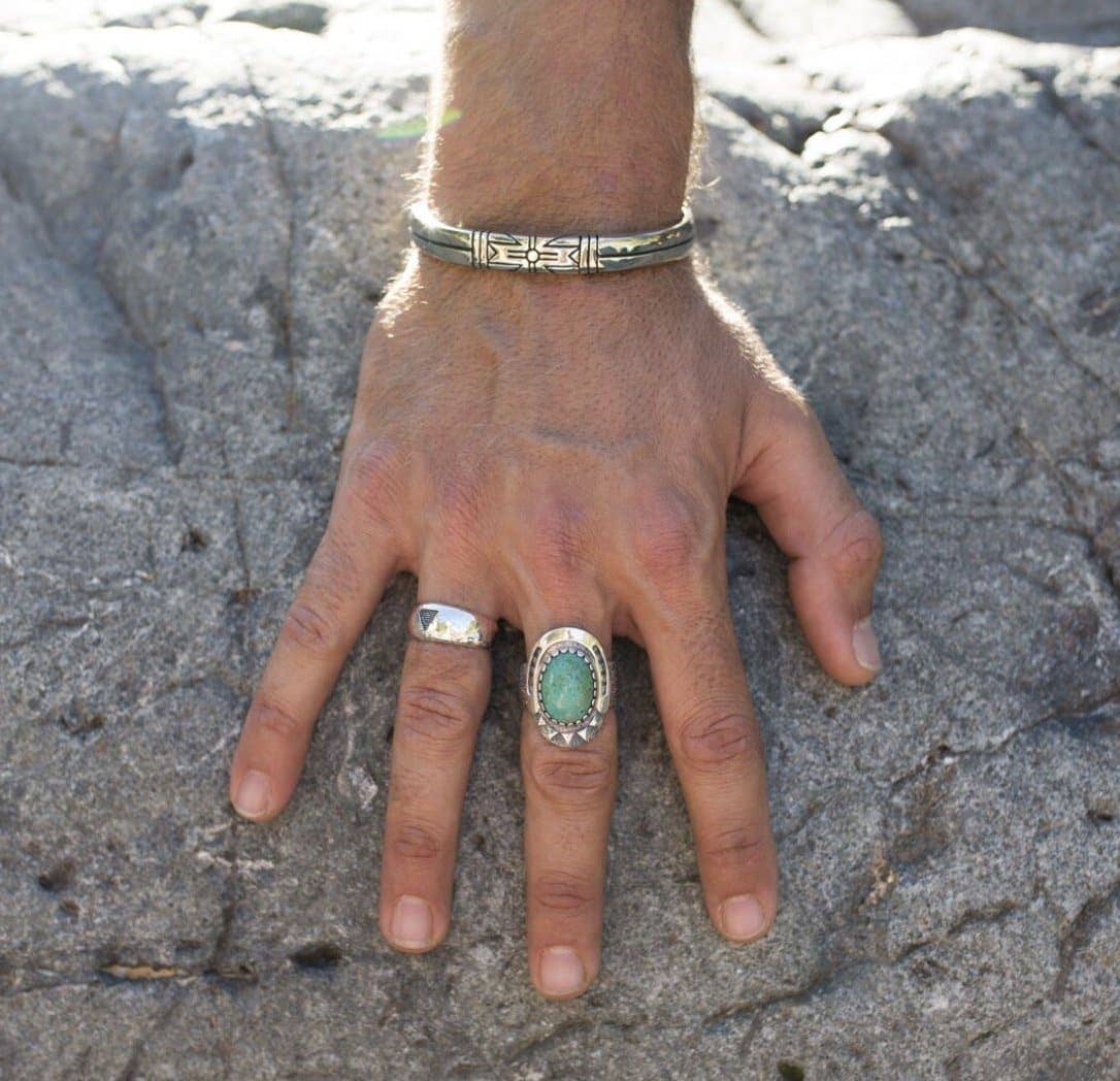 Hand wearing Medicine Wheel Cuff || Men with rings resting on textured rock surface in natural light