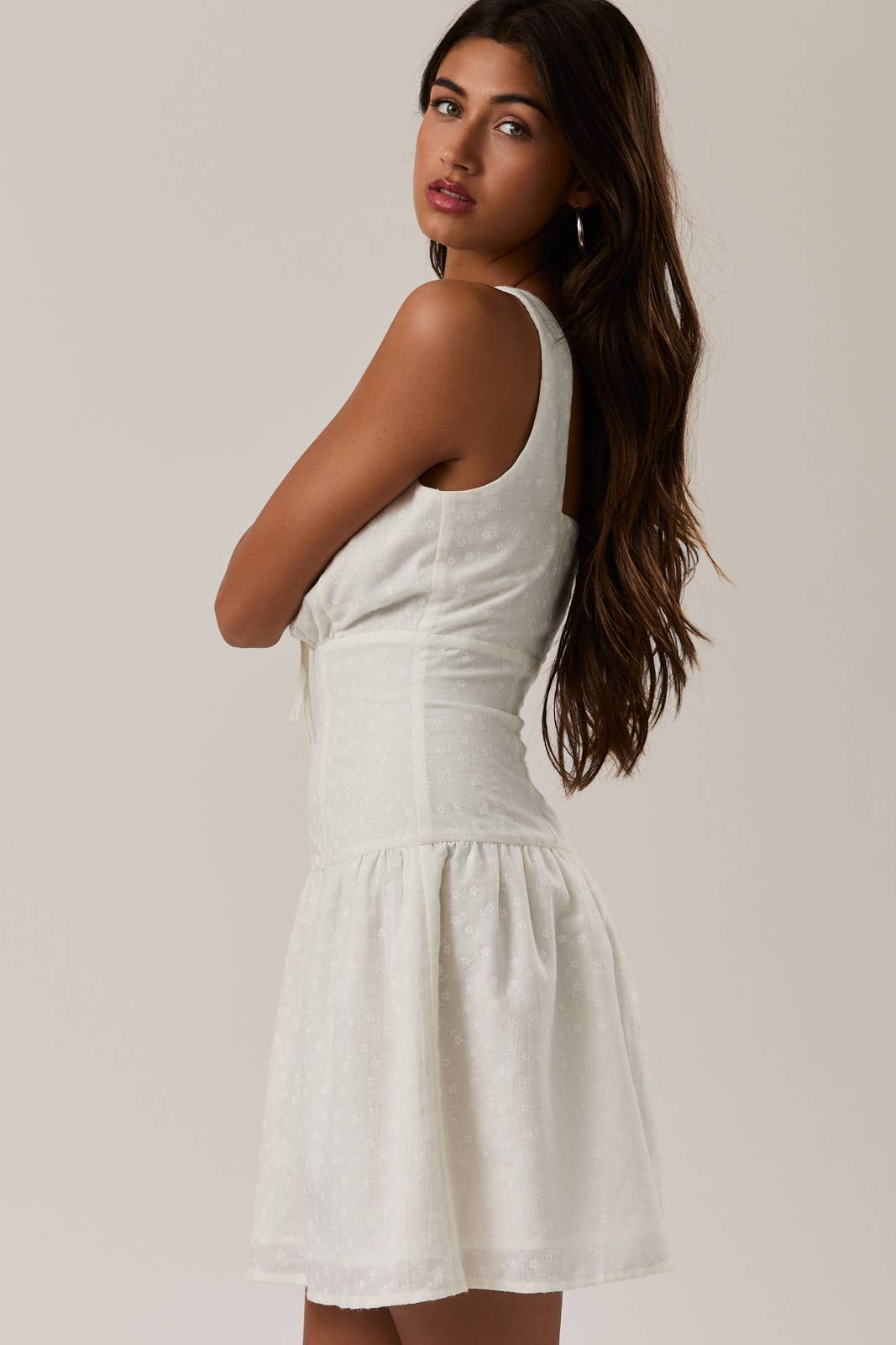 Woman wearing a white Shirred Neck Low Waist Mini Dress with textured fabric and sleeveless design, posing sideways.