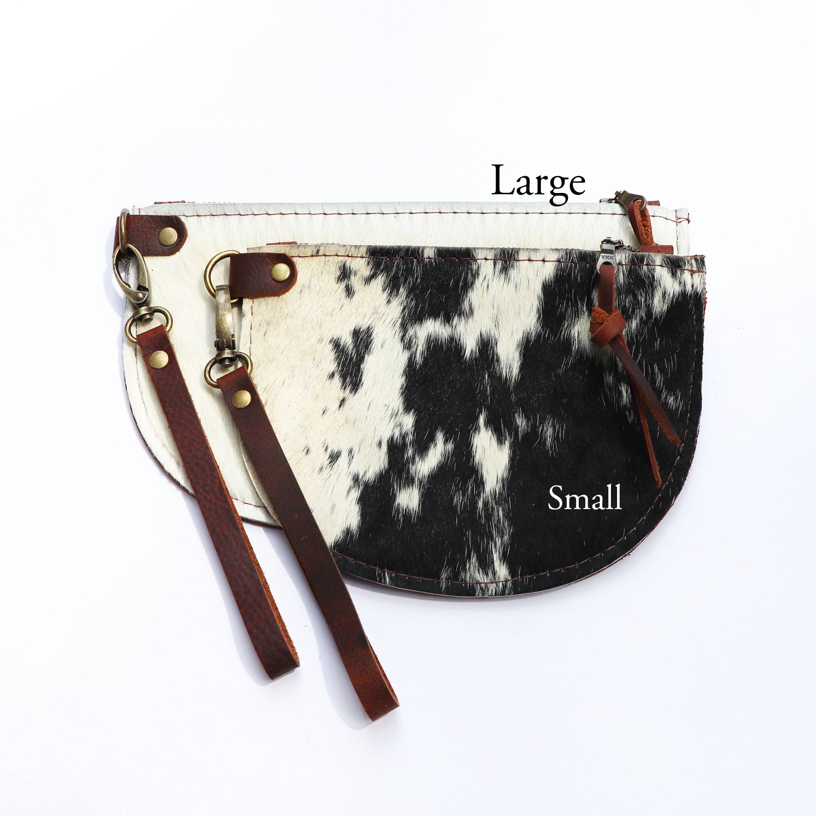 The Hawks & Doves Large Half Moon Cowhide and Leather Zip Pouch with Wristlet, crafted from black and white cowhide leather with a detachable wristlet, is shown overlapping with a smaller matching pouch on a white background.