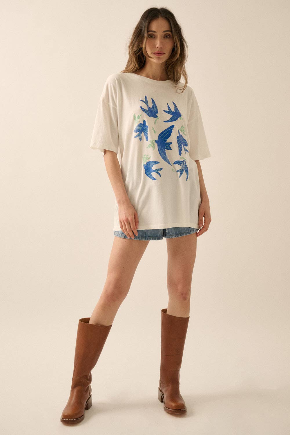 Woman wearing Vintage Birds Garment Washed Oversized Graphic Tee with blue bird designs, denim shorts, and brown boots