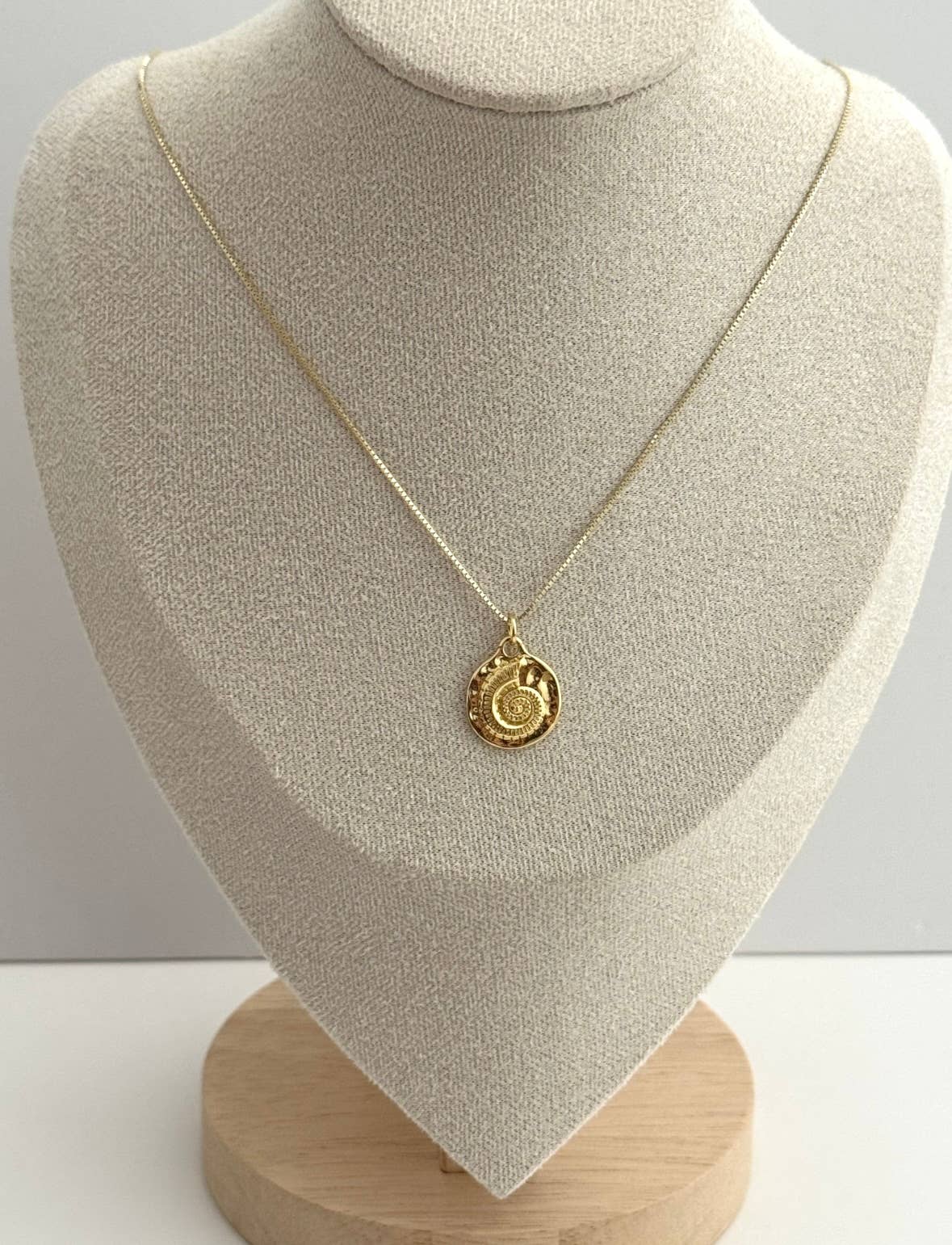 The Mar Medallion Necklace by Tramps+Thieves, featuring a delicate gold vermeil chain and round engraved pendant, is shown on a beige fabric-covered jewelry bust with a wooden base.