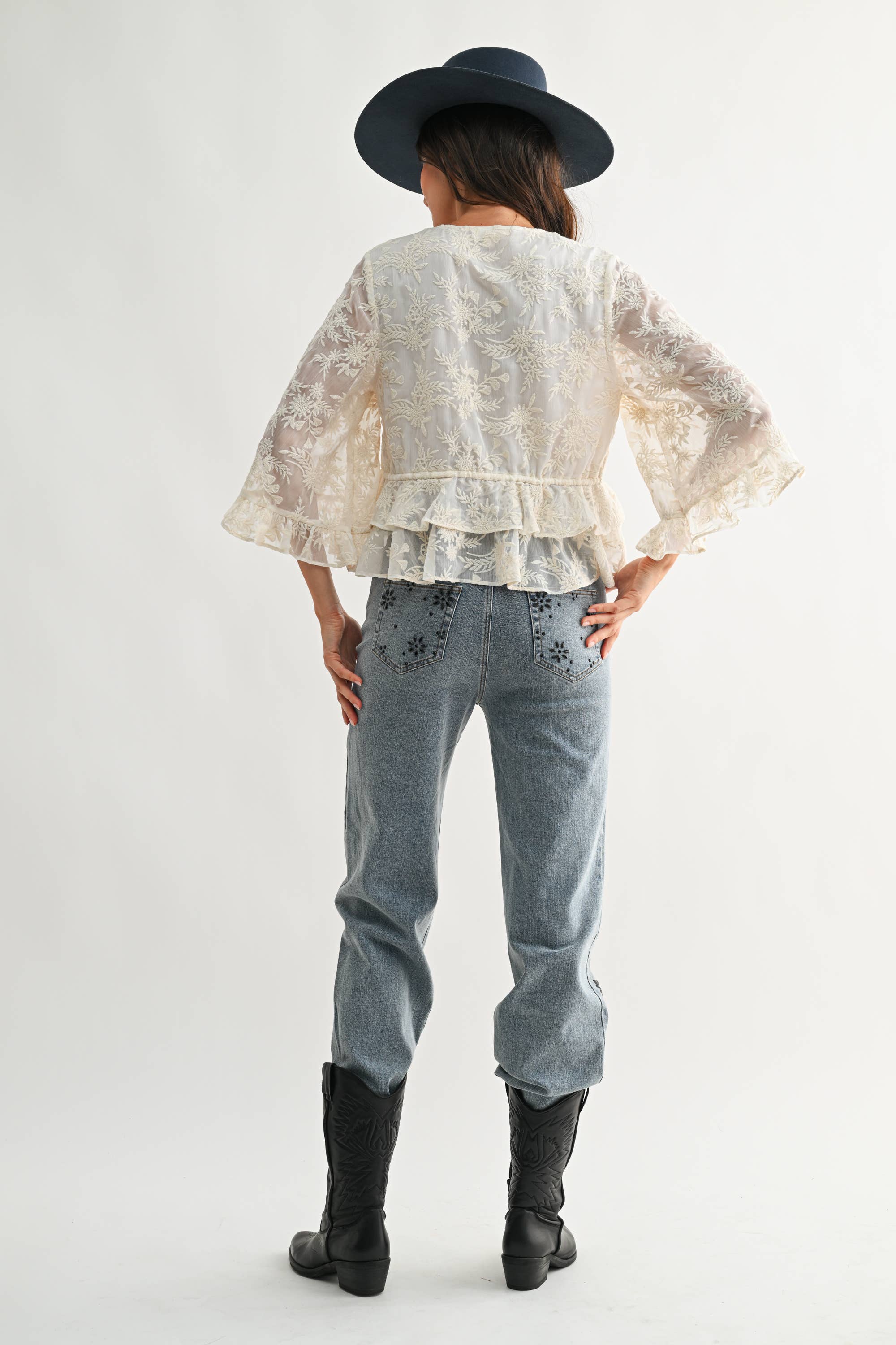 Woman wearing a Boho Embroidered Sheer Blouse with flared sleeves paired with light denim jeans and black boots.