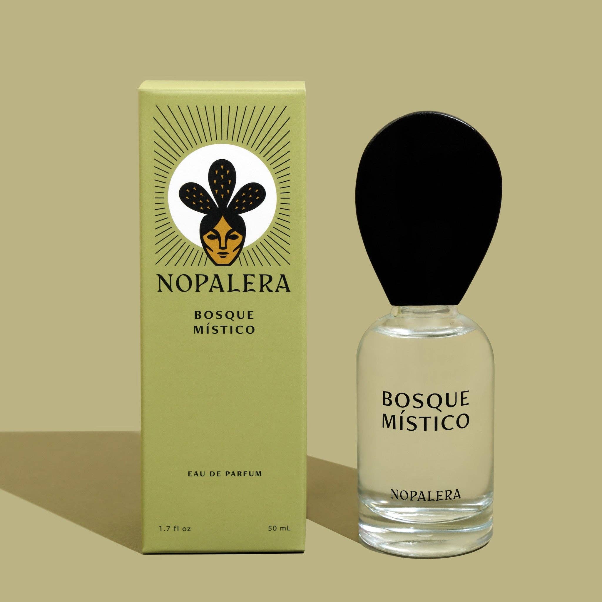 A 10mL Nopalera Bosque Místico Eau de Parfum Travel Spray stands by its green box, adorned with a stylized face and leaf motifs. This clean scent evokes Mexicos mystical forests and features a black cap with minimalist branding.