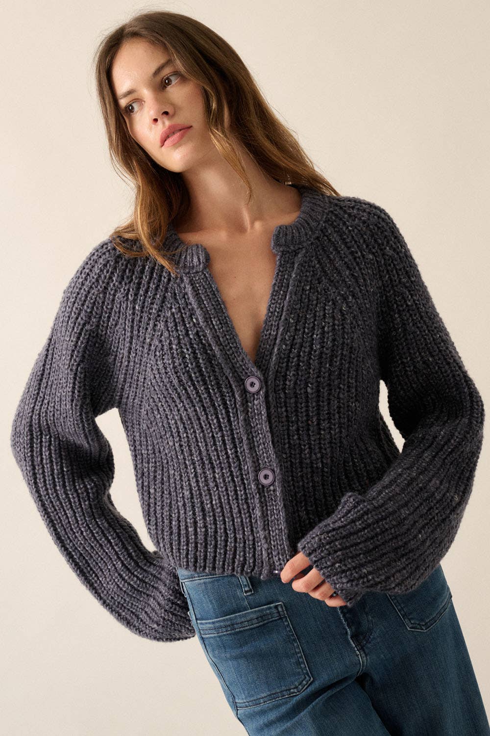 A woman with long brown hair wears the Promesa USA Confetti Button-Front Cardigan Sweater in dark gray and blue jeans, standing against a light beige background.