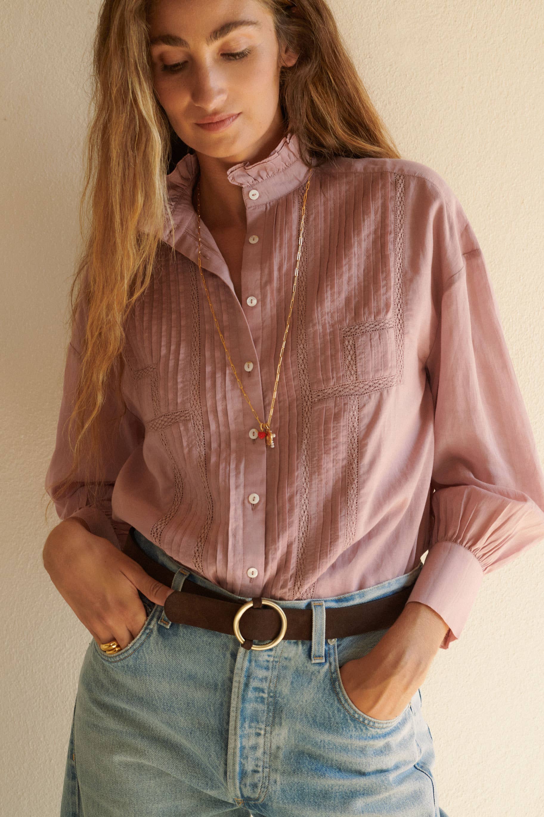 Wearing the Alexa Blouse Rose by Sonmer Shop USA—light pink voile with lace trim and stitching—tucked into high-waisted light blue jeans and a dark belt, this look against a neutral wall is perfect for fall layering.