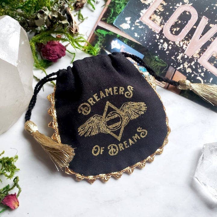 Black drawstring pouch with gold tassels and "Dreamers of Dreams" text holding Opal Moon Halo Hoop Earrings