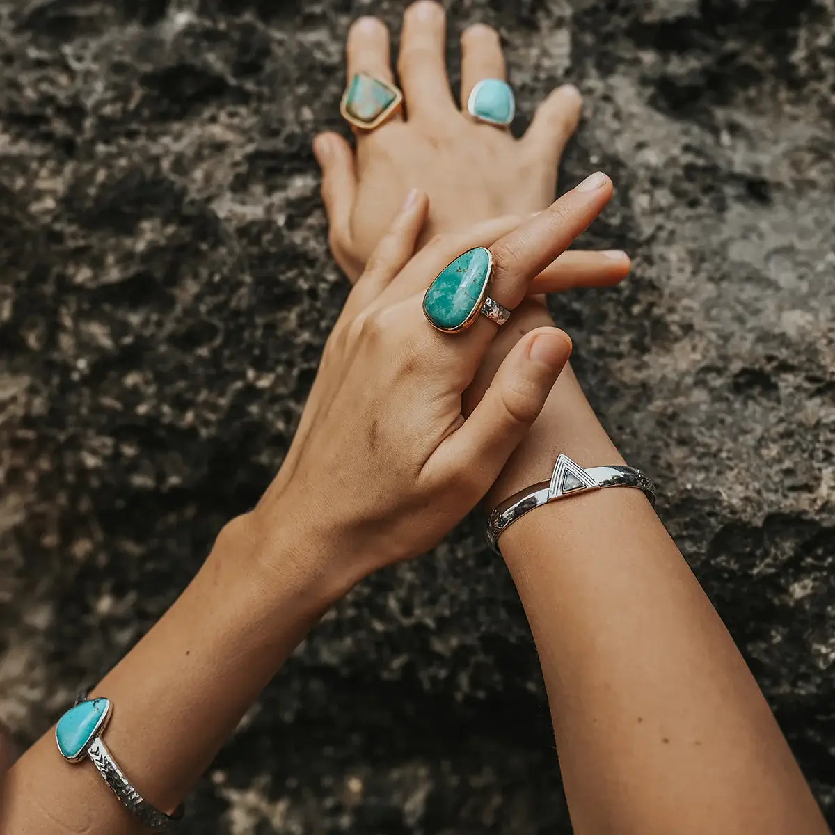 Hold Space Cuff on wrist with turquoise rings, styled on hands against a natural textured stone background