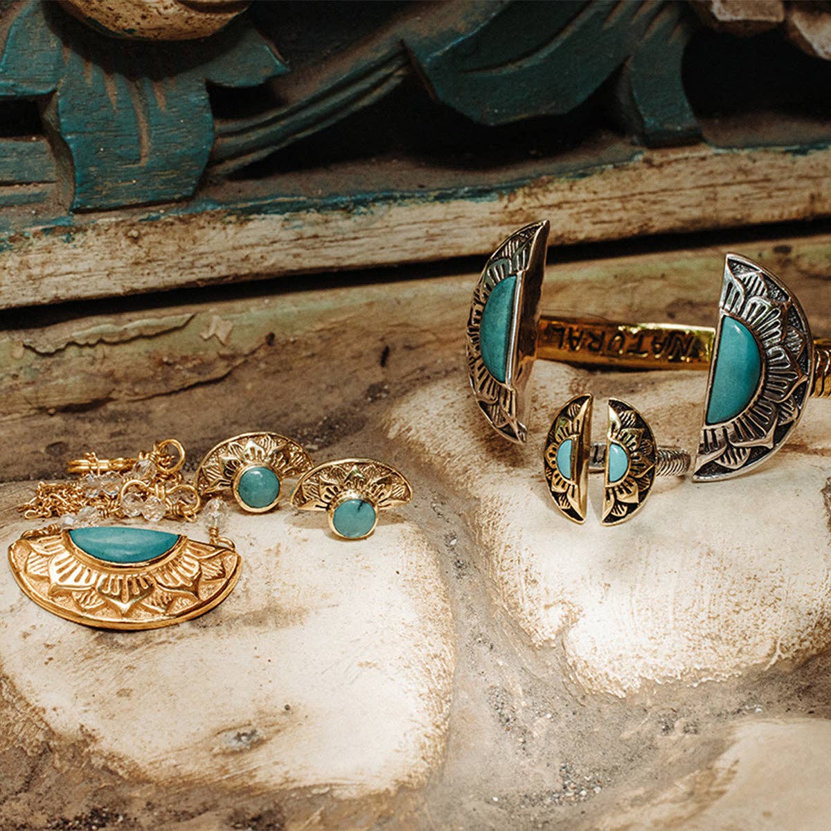 The bahgsu jewels Natural Mystic Ring - Turquoise is showcased with a matching necklace, earrings, and cuff bracelet on a rustic wooden surface with intricate carved details in the background.