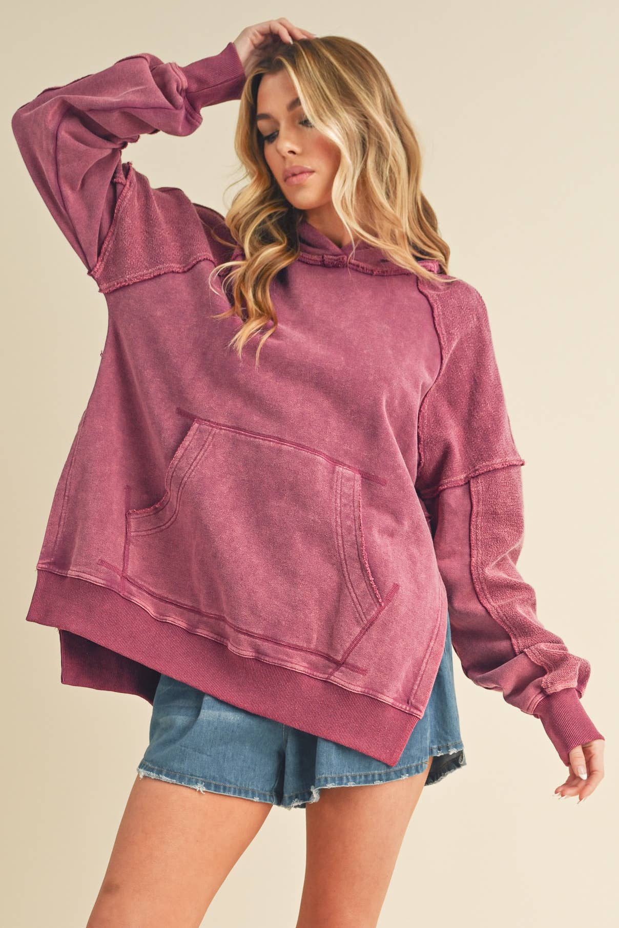 Woman wearing a faded pink Deb Washed Hoodie with front pocket and casual long sleeves paired with denim shorts