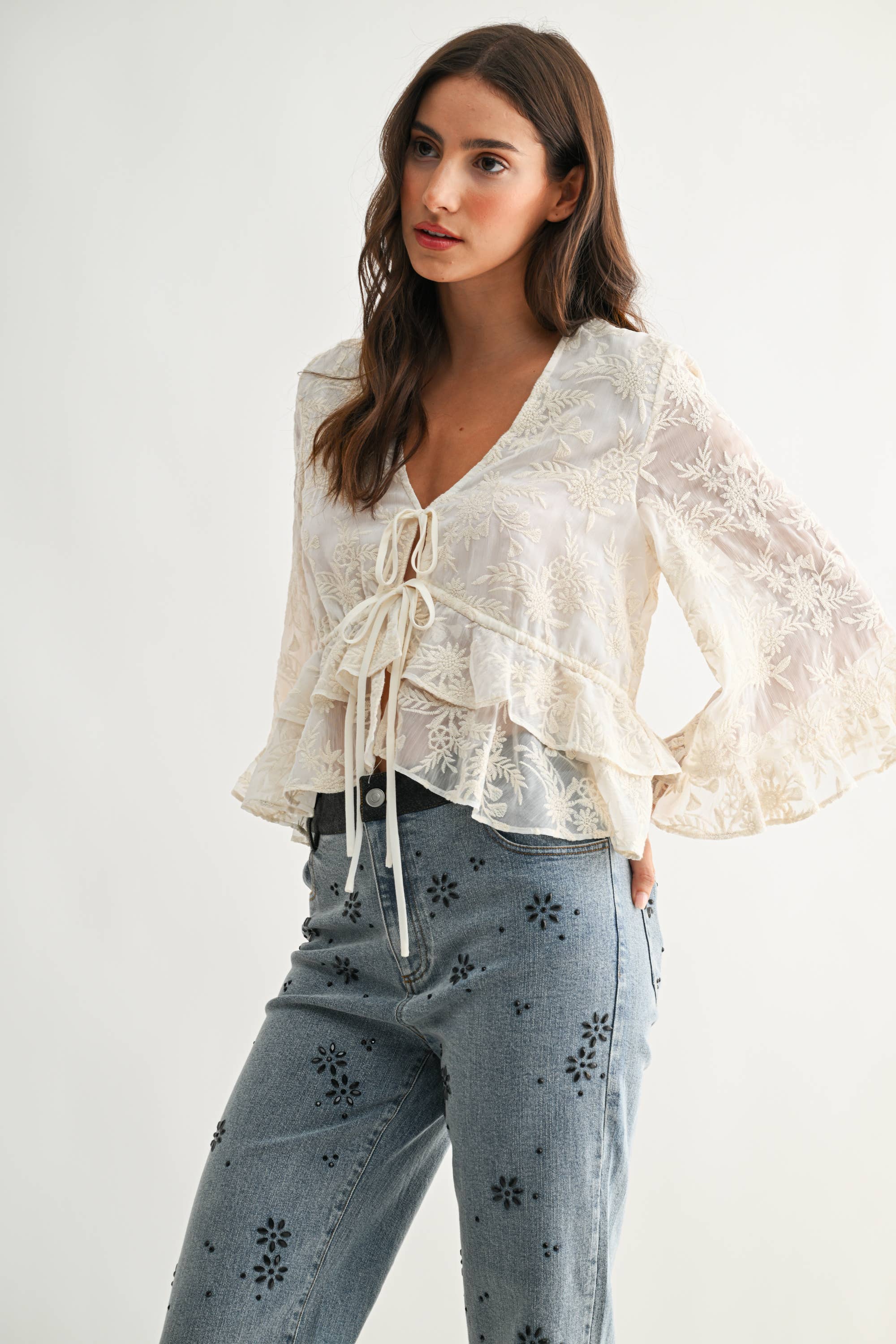 Woman wearing a Boho Embroidered Sheer Blouse with floral pattern and tie front, paired with printed denim jeans.