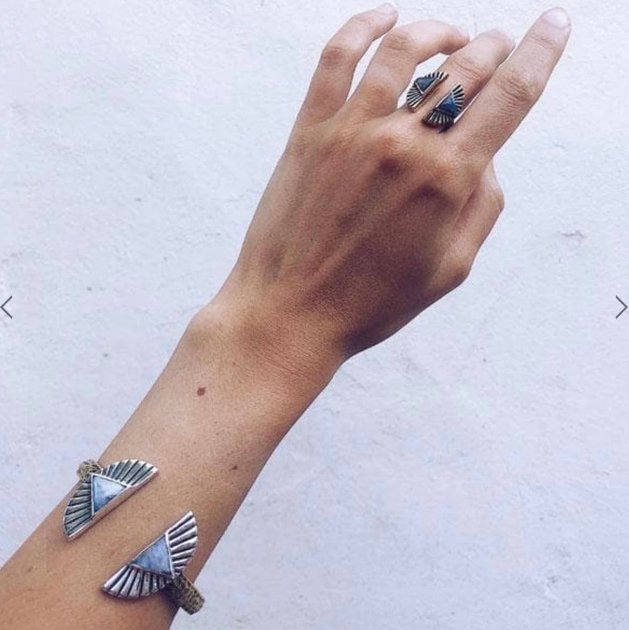 A hand wears the bahgsu jewels Shape Shift Ring and a matching open cuff with geometric triangle and fan motifs, set against a light grey textured background.