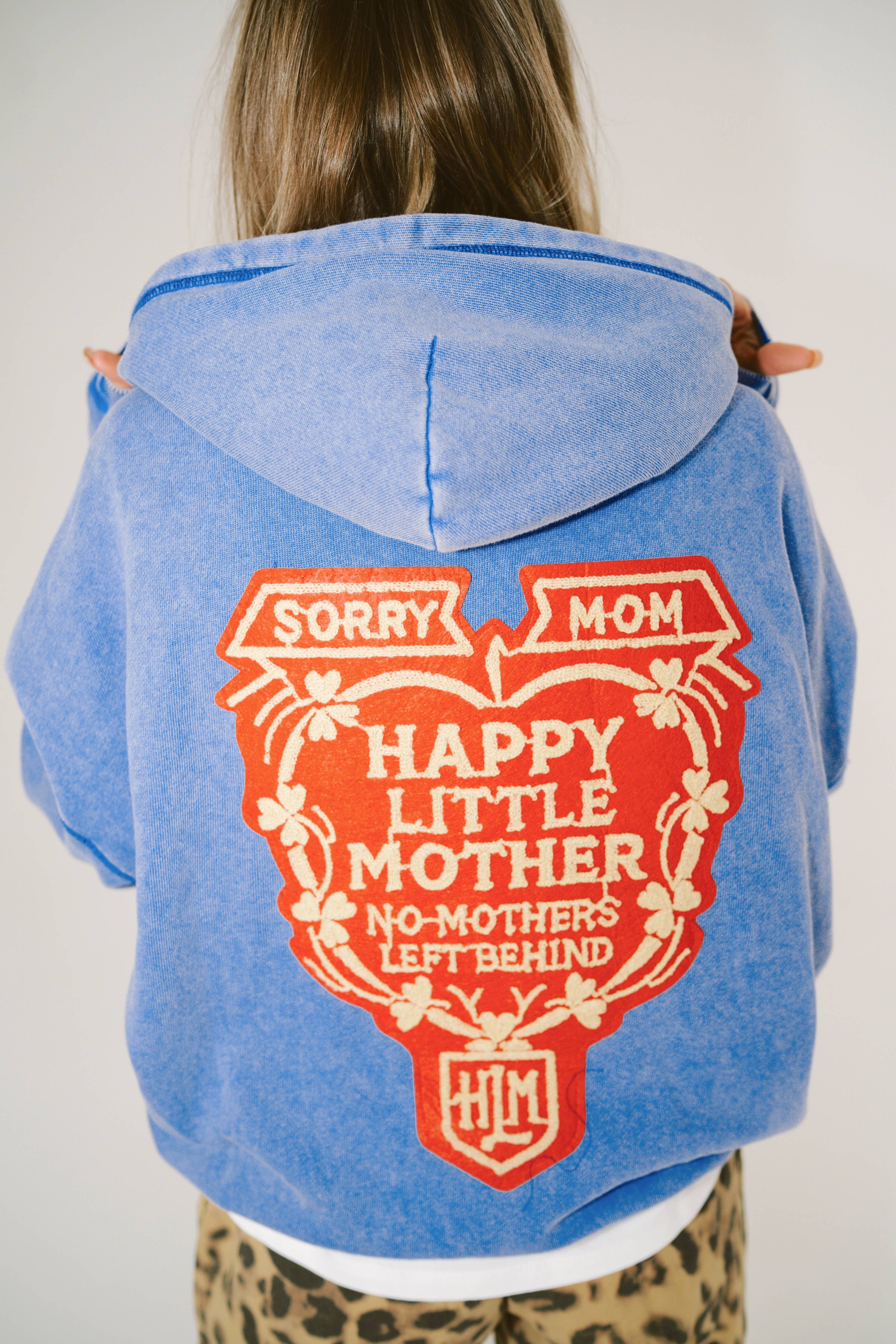 Back view of person wearing blue SORRY MOM HOODIE - PRESALE with large red and cream graphic design on back