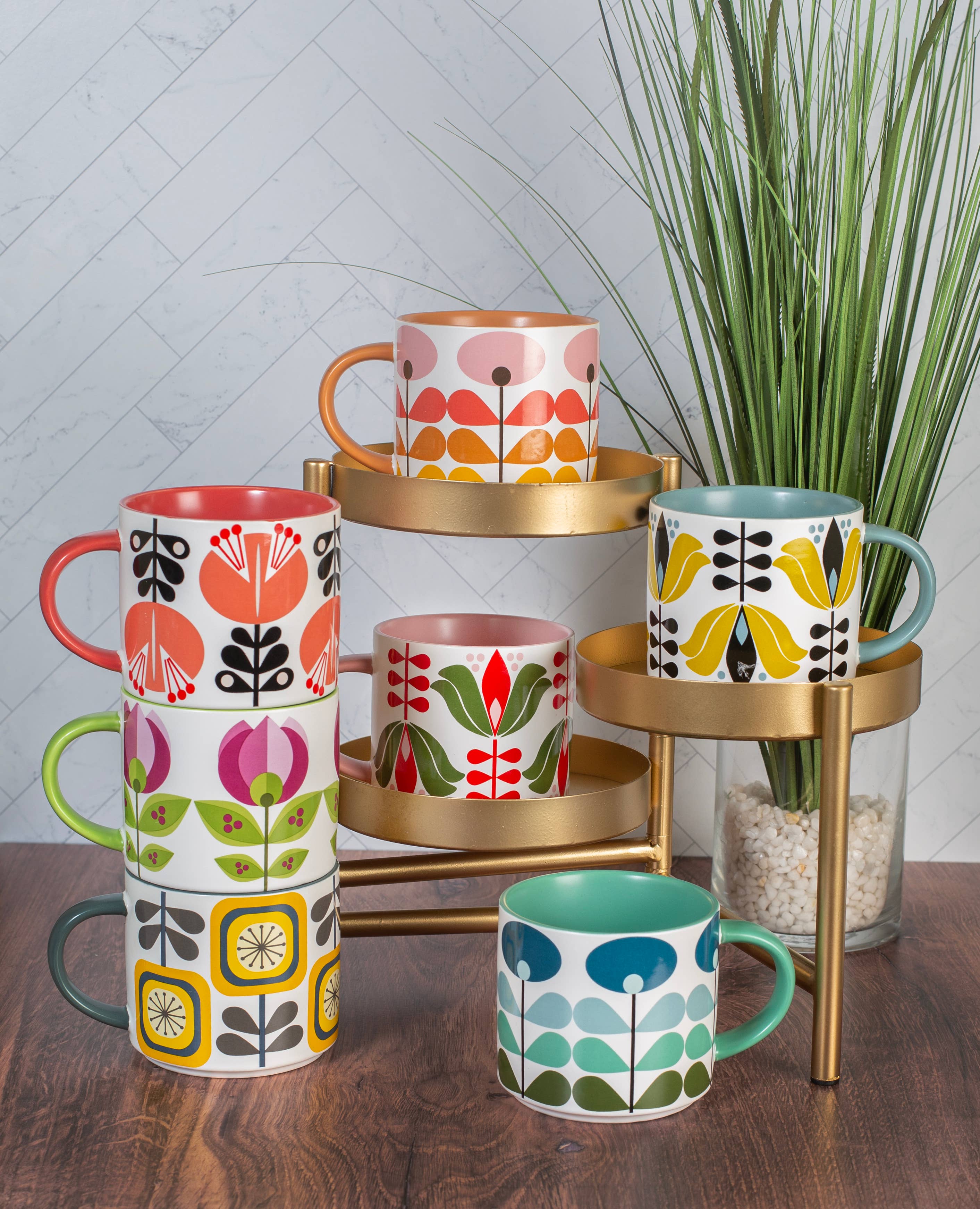 Sunflower Fall Mid Century Modern Stackable Matte Coffee Mug collection with colorful floral designs on a display stand with plant background