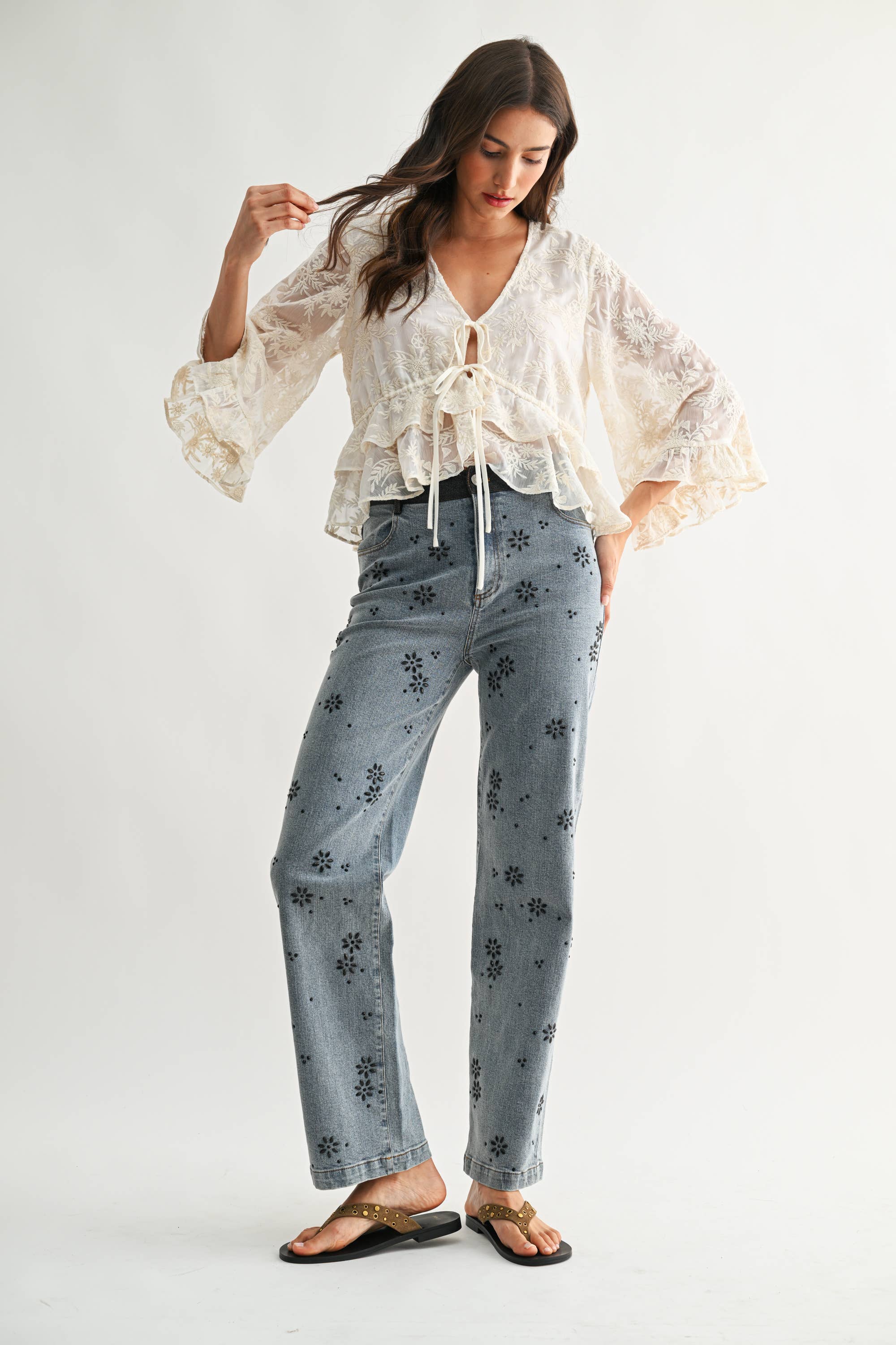 Woman wearing Boho Embroidered Sheer Blouse with flowy sleeves paired with floral patterned jeans and sandals.