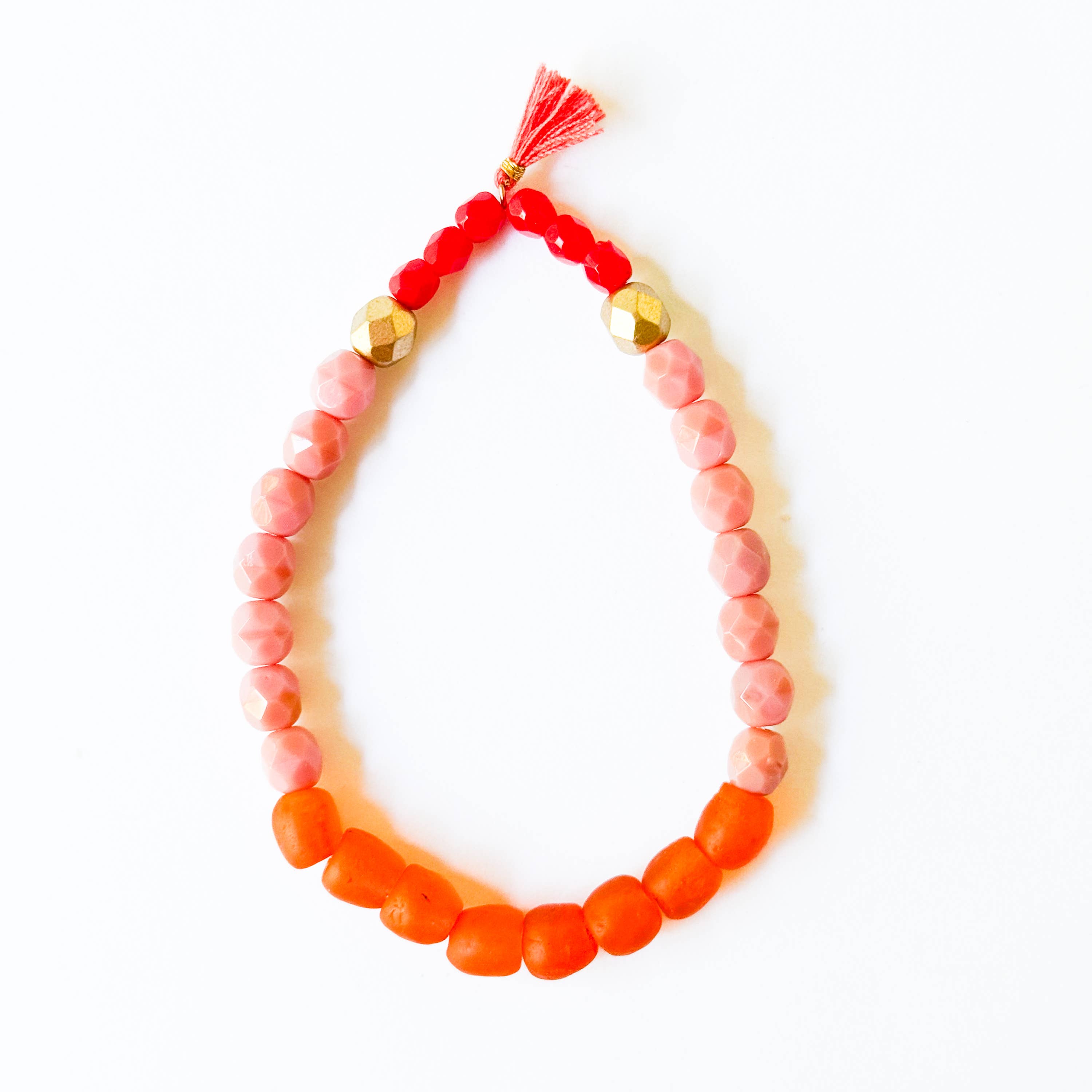 Multicolor Recycled African Glass And Mixed Bead Bracelet with red tassel and gold accent beads on a white background