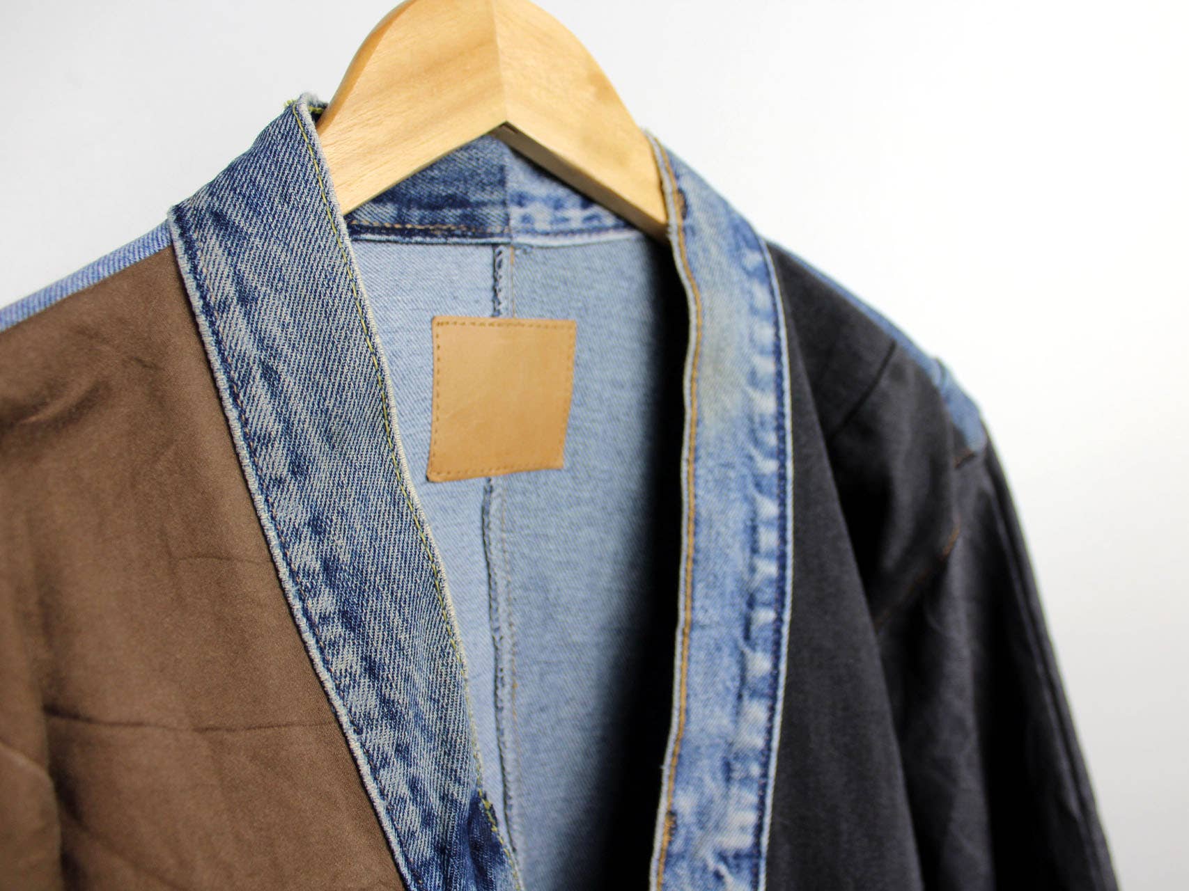 Close-up of a hanging Upcycled Patchwork Denim Jacket showing the mix of denim and fabric panels on a wooden hanger.