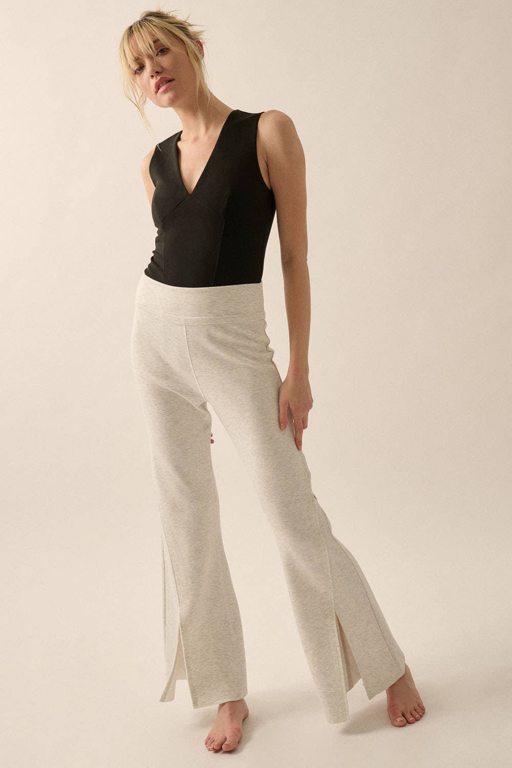 Woman wearing Essential Trends Crepe V-Neck Bodysuit in black paired with light beige split-hem pants, standing barefoot.