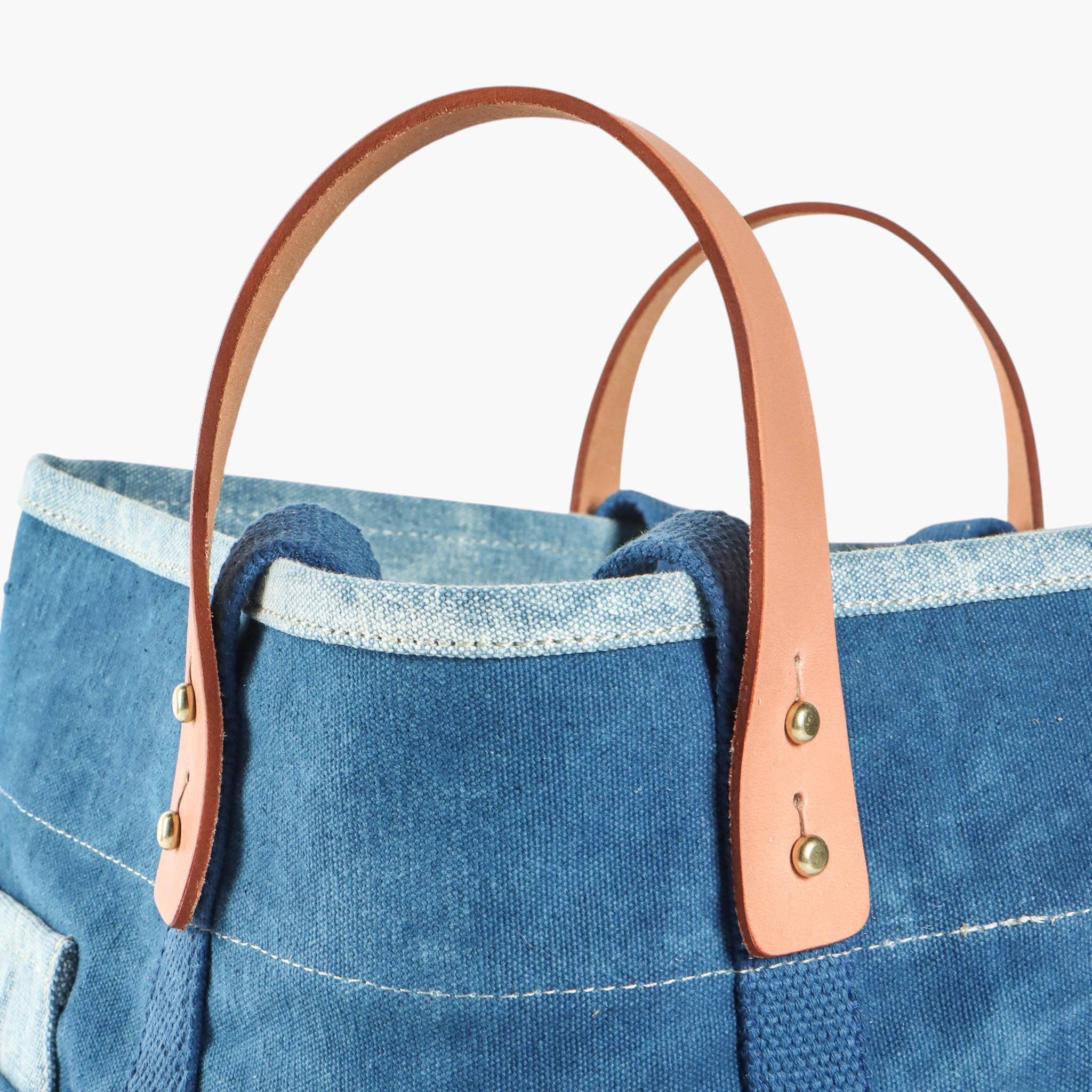 Blue denim tote bag with brown leather handles on a light blue background