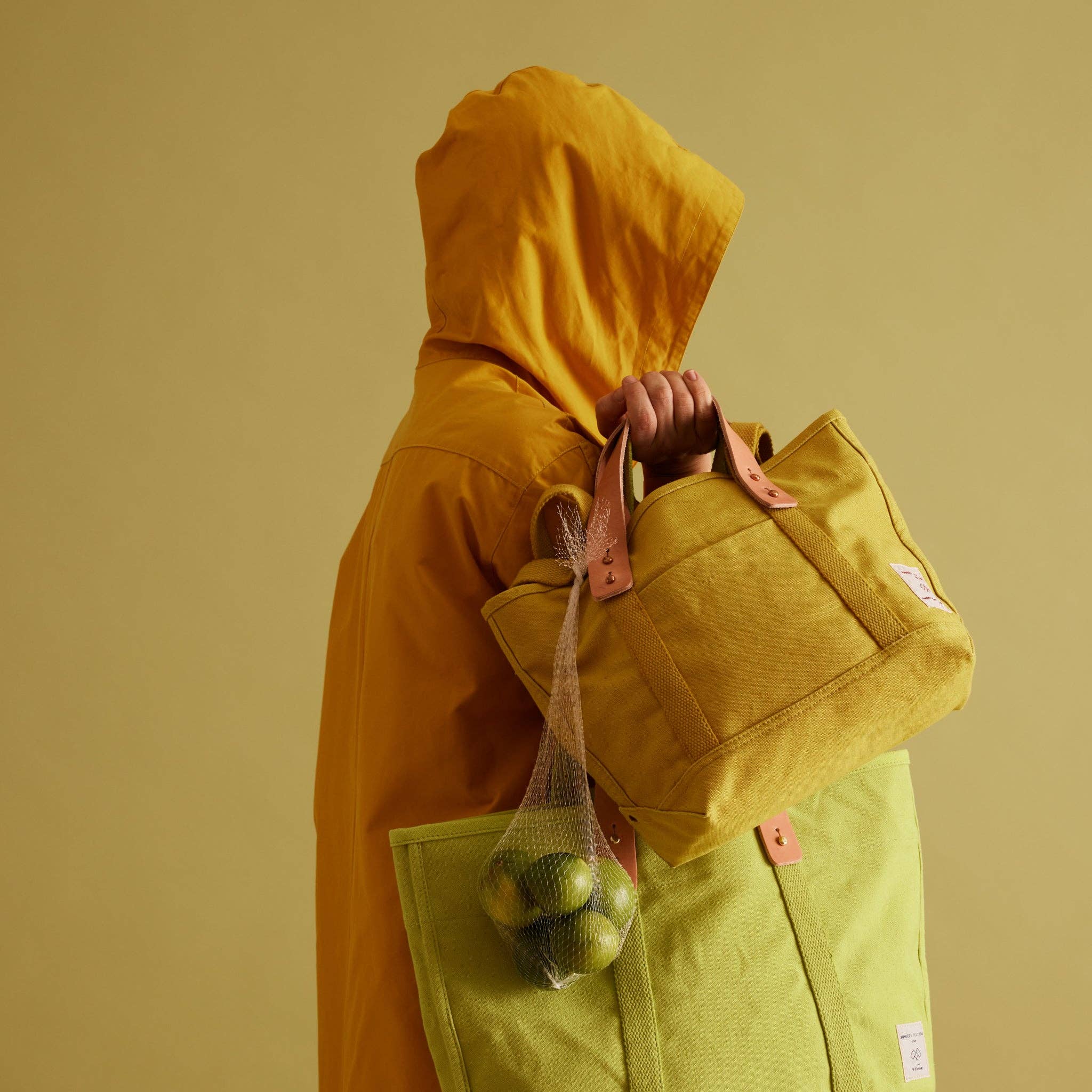 Person in yellow hooded jacket holding Lunch Tote | Chartreuse with another green tote and net bag of limes