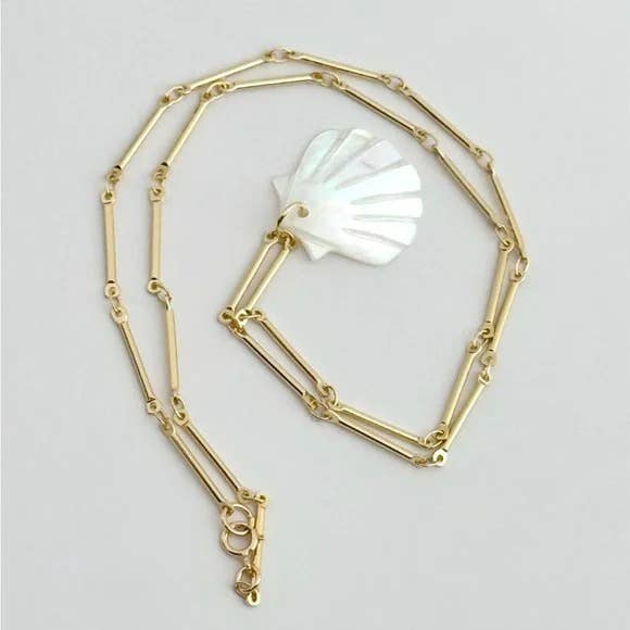 The Muna Shell Necklace by Tramps+Thieves features a gold chain with elongated links and a glossy, iridescent shell-shaped mother of pearl pendant, displayed on a plain light background.