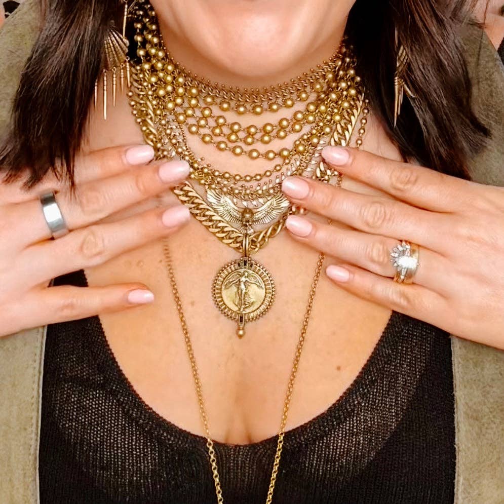Woman wearing layered gold necklaces featuring the Icaria Eagle Necklace Antique Gold with matching jewelry and rings