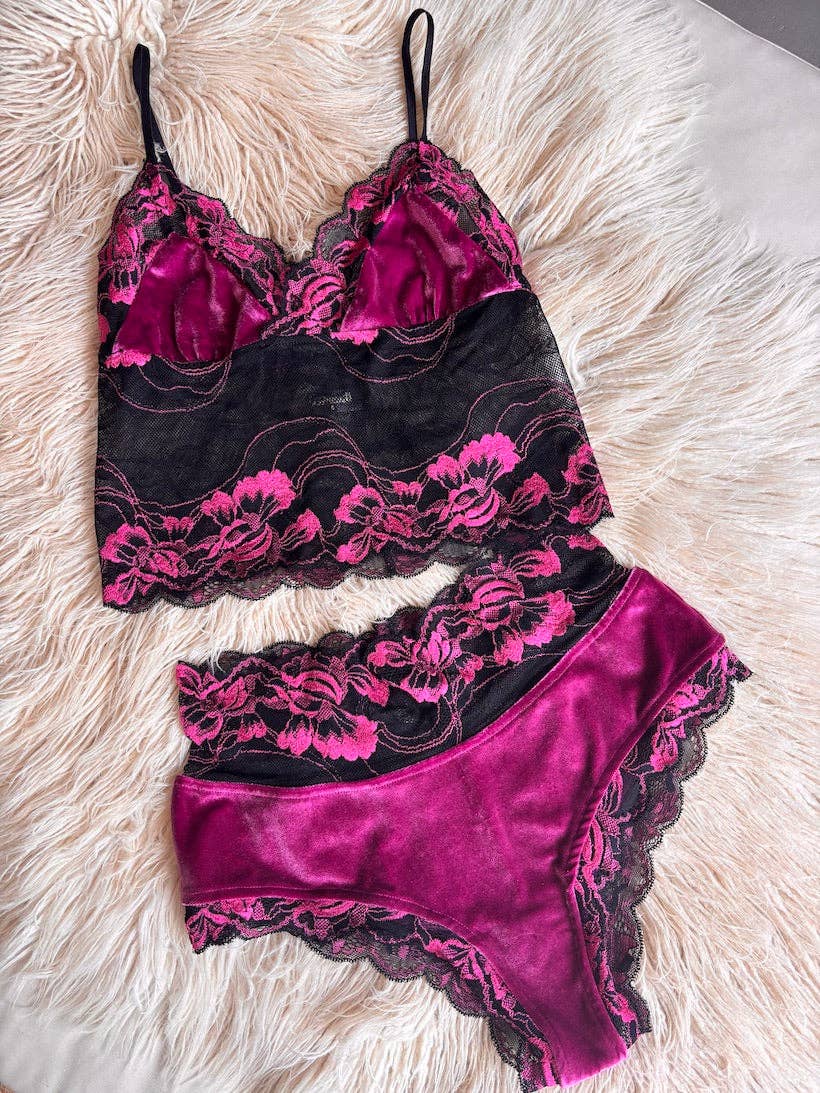 The Kultcha Collective Fuchsia Velvet & Lace Bralette, paired with matching high-waisted panties, features black and magenta floral stretch lace and is displayed on a soft, light-colored furry surface.