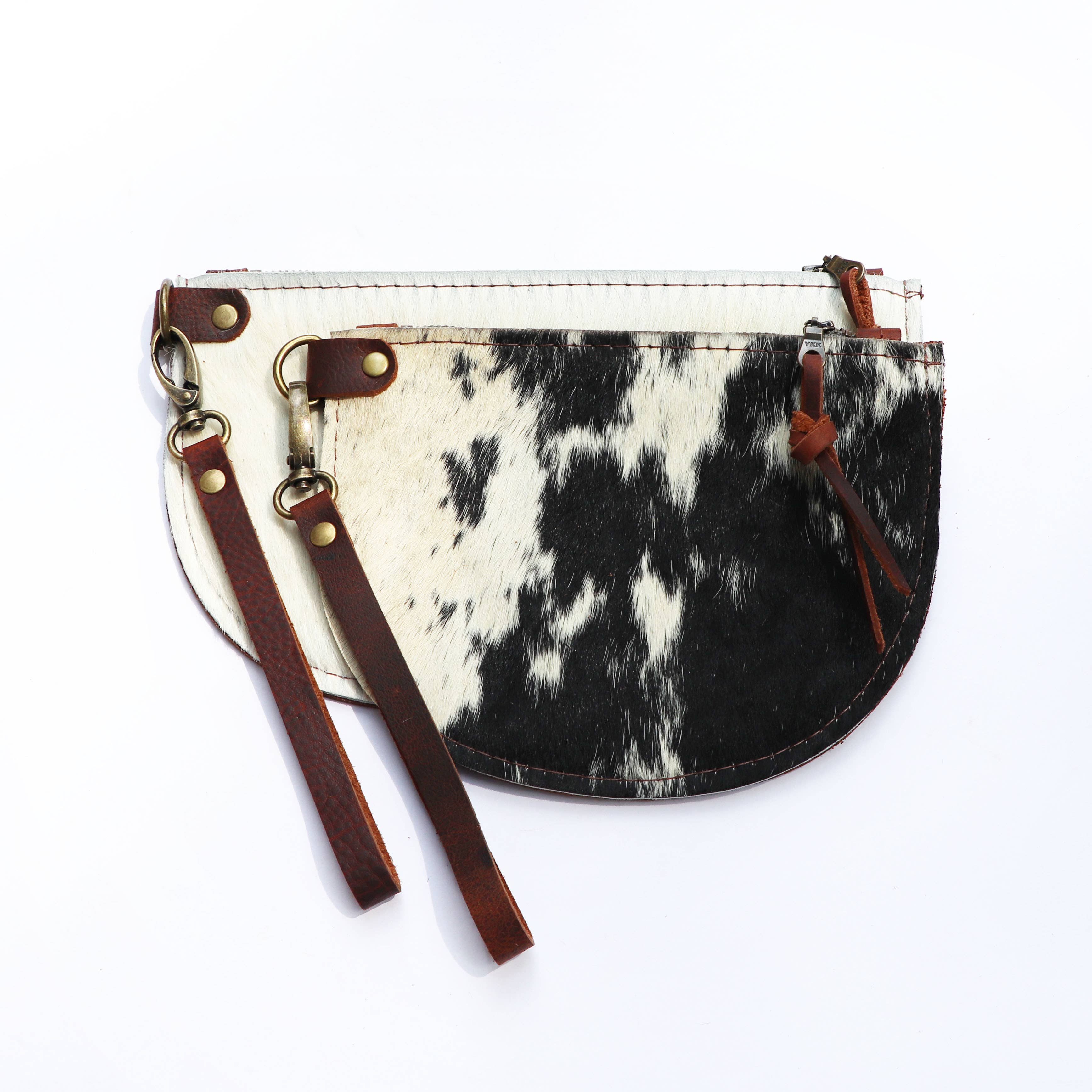 Two Hawks & Doves Large Half Moon Cowhide and Leather Zip Pouches feature black and white patterns, brown leather zipper pulls, and detachable wristlet straps, displayed against a white background.