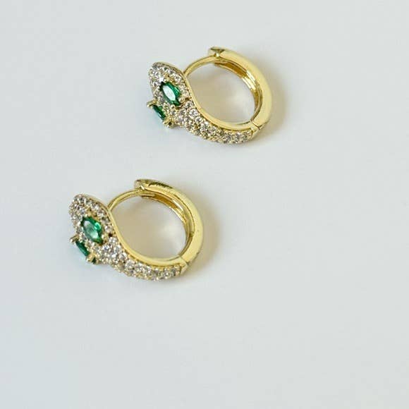 The Tramps+Thieves Diamond Snake Huggies are gold-plated brass serpent earrings with clear crystal accents and emerald cubic zirconia eyes, shown on a white background.