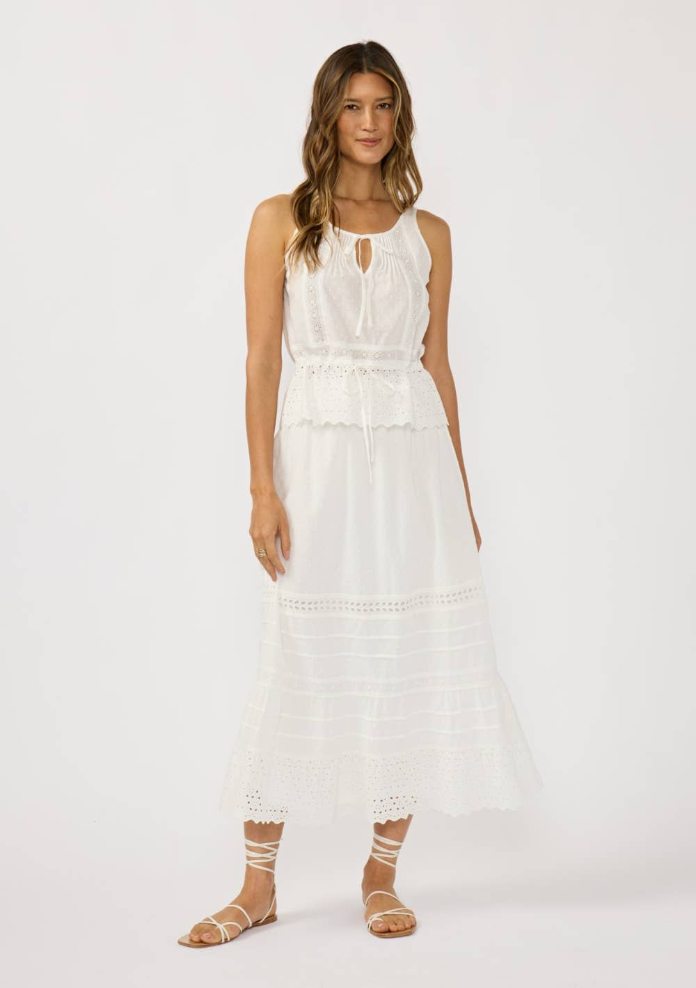 Woman wearing a white Eyelet Hem Pintuck Skirt with matching sleeveless top and strappy sandals in a bright studio.