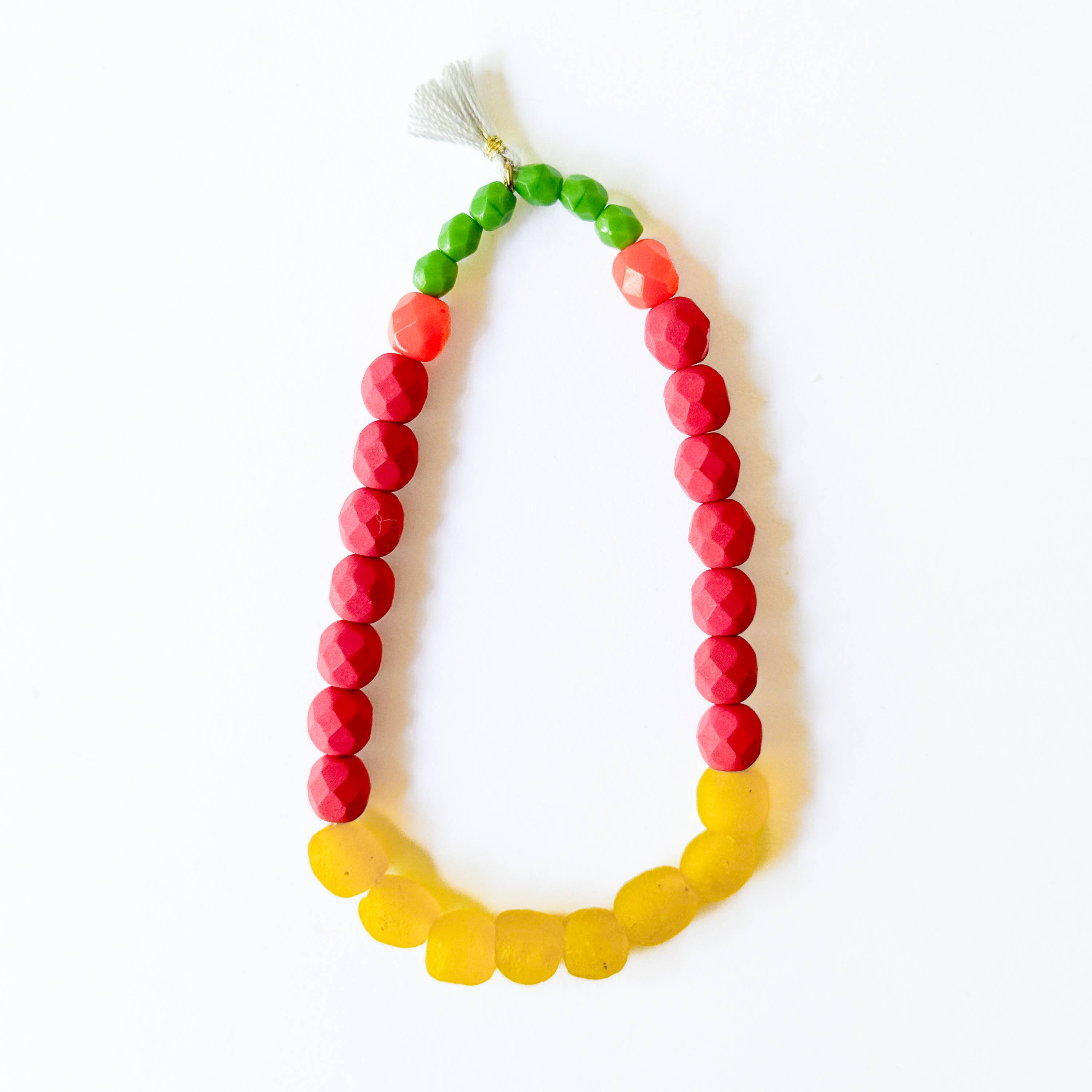 Multicolor Recycled African Glass And Mixed Bead Bracelet with green, red, orange, and yellow beads and a small tassel charm