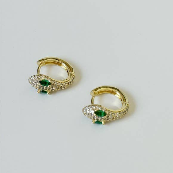 The Diamond Snake Huggies by Tramps+Thieves are gold-plated brass earrings with clear stones and emerald cubic zirconia eyes, beautifully displayed against a plain light background.