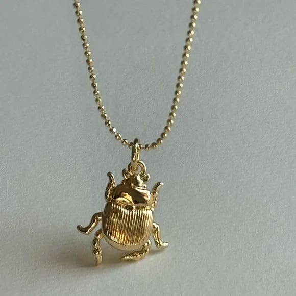 The Scarab Necklace by Tramps+Thieves features a gold-filled beetle-shaped pendant with detailed legs and a ribbed body, shown against a light neutral background.