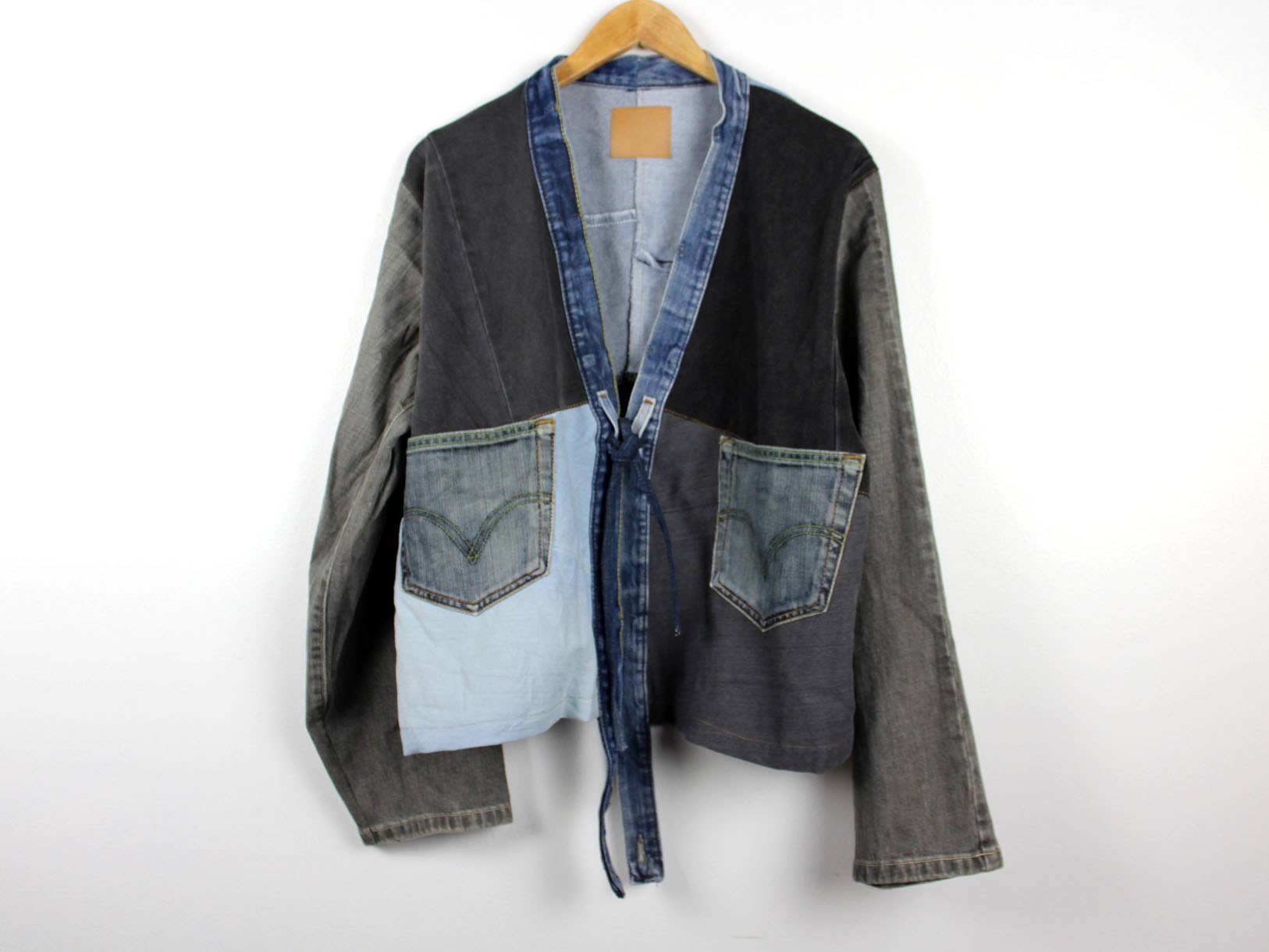 Upcycled Patchwork Denim Jacket with mixed denim shades and front pocket details hanging on wooden hanger