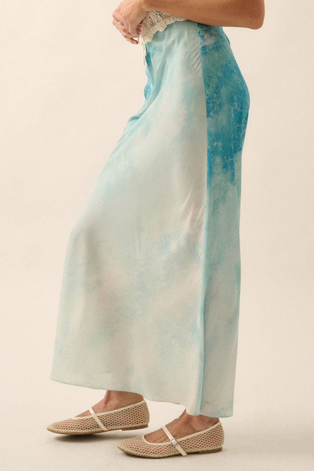 Side view of a light blue Tie Dye-Print Satin Bias-Cut Maxi Skirt paired with cream woven flats