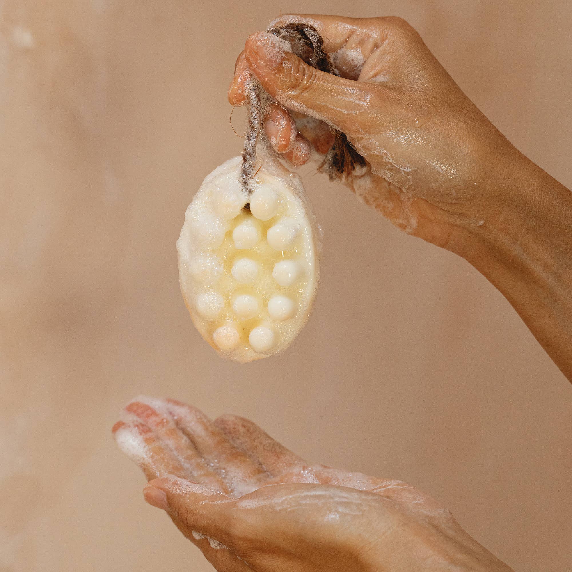 A person holding Cedar and Myrrh’s Palo Santo + Shea Butter Bar Soap with embedded beads in one hand, washing the other—ideal for sensitive skin.