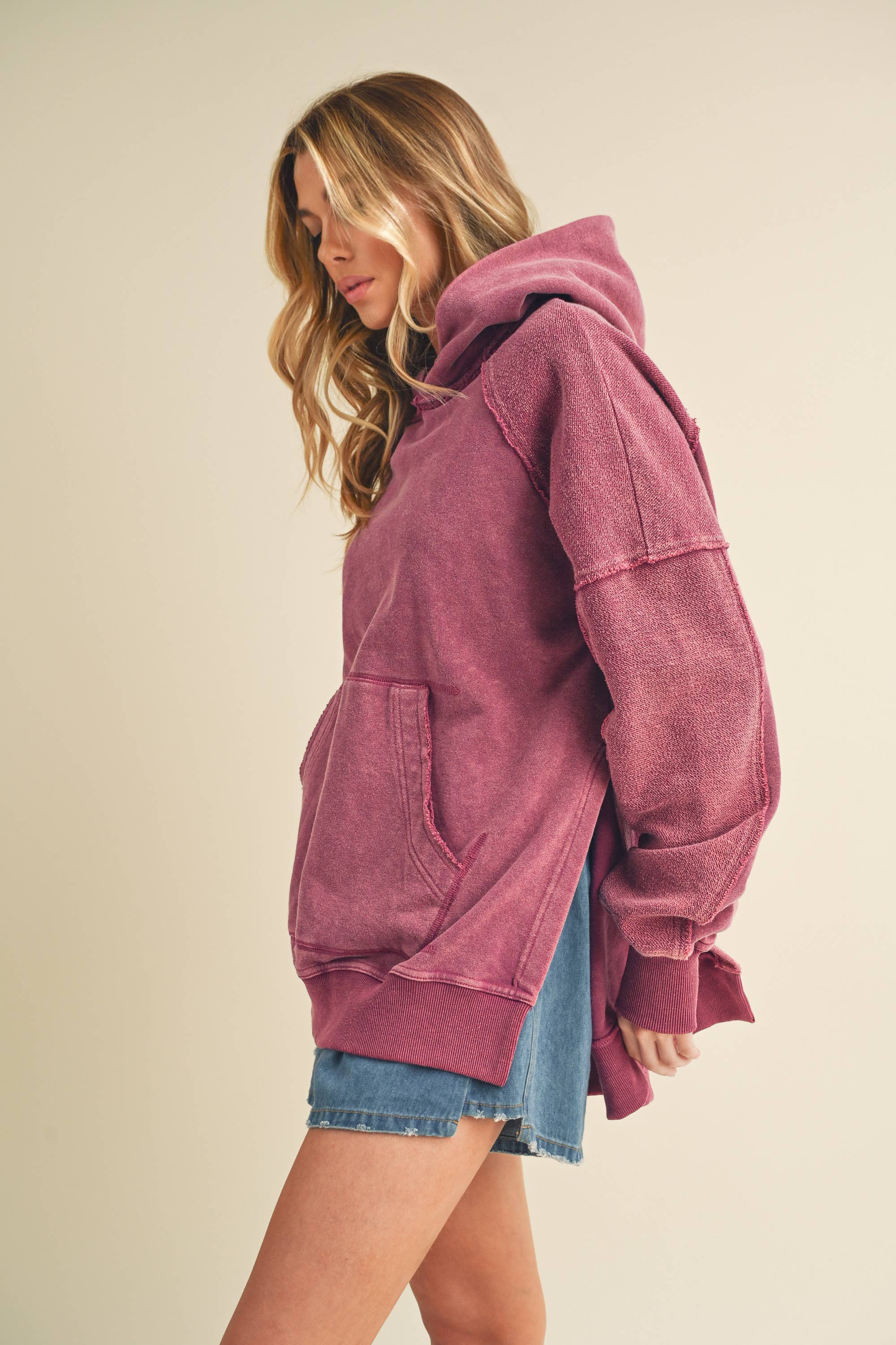 Woman wearing a relaxed fit faded pink Deb Washed Hoodie paired with denim shorts against neutral background