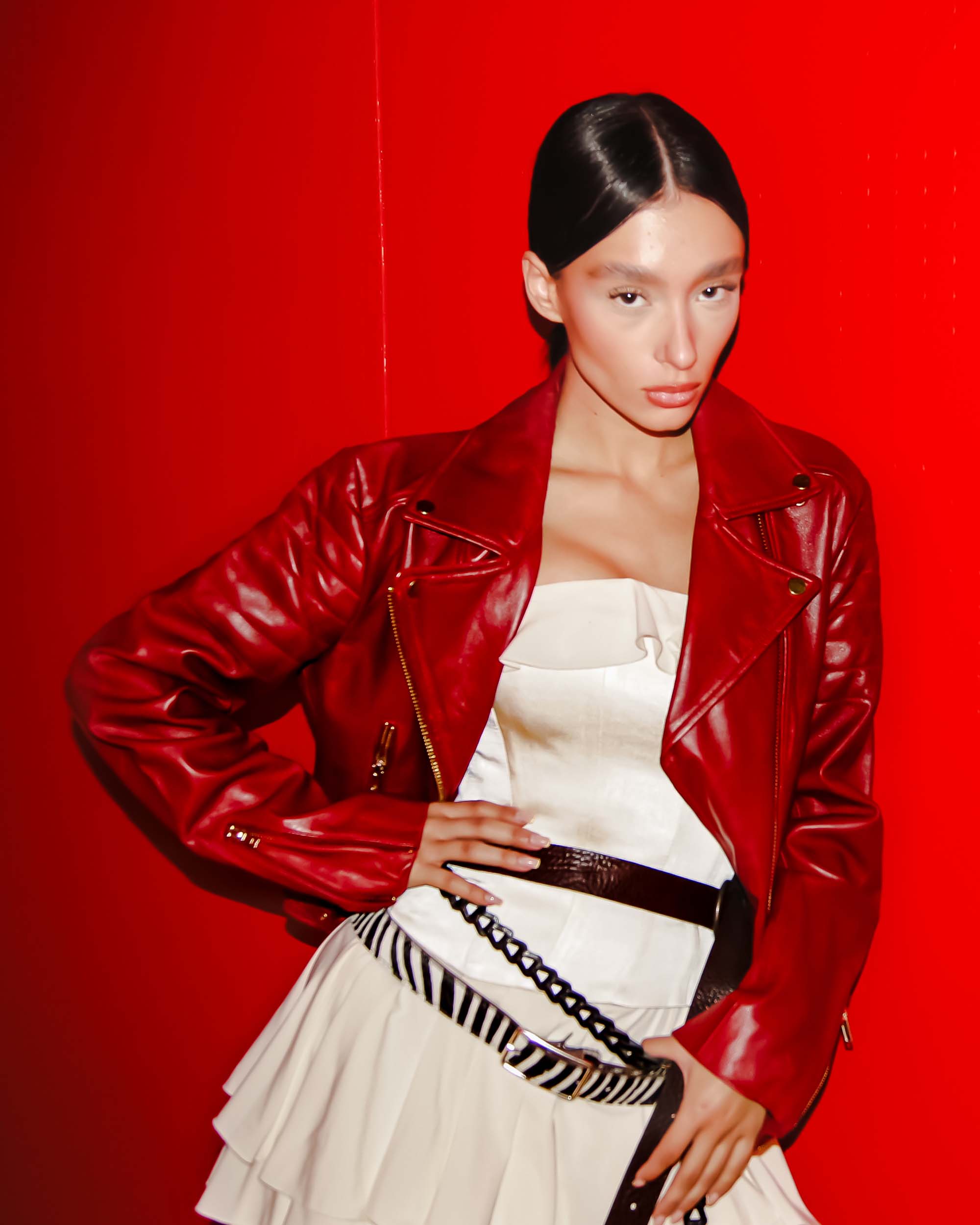 Model wearing Eureka | Leather Biker Jacket in vibrant red over a white dress with belt against red background