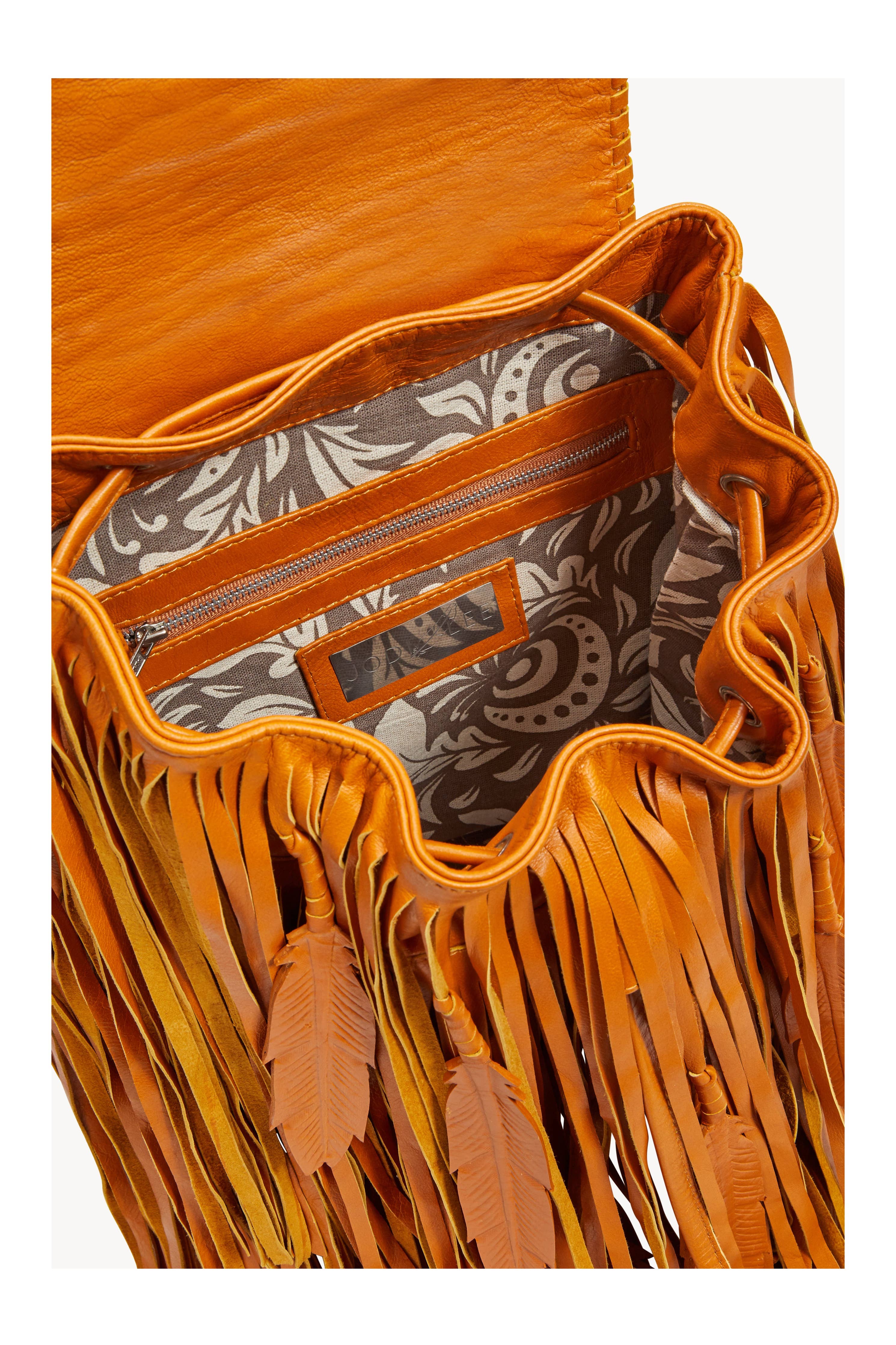 The Jodi Lee Monterey Backpack in Antique Tan features an open-top design, hand-painted leather with feather-shaped tassels, gray and white patterned fabric lining, an interior zip pocket, and a leather-trimmed slip pocket.
