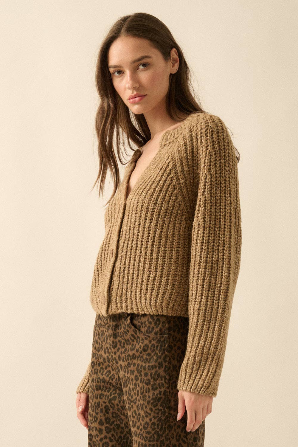 A woman with long brown hair wears the Promesa USA Confetti Button-Front Cardigan Sweater and high-waisted brown leopard print pants, standing against a plain beige background.