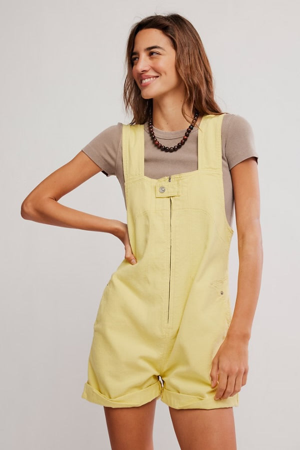 Woman smiling wearing yellow Free People Jude Shortall Overall Short over a beige short-sleeve top with a beaded necklace