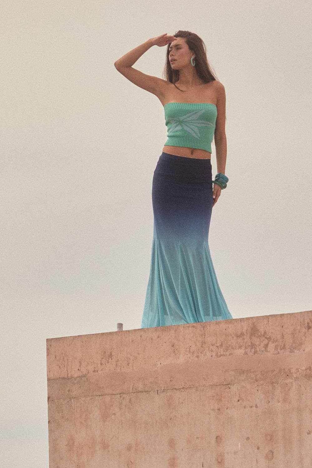 Woman wearing Ombre Mesh Fit-and-Flare Godet Maxi Skirt in gradient blue standing on rooftop with hand shielding eyes